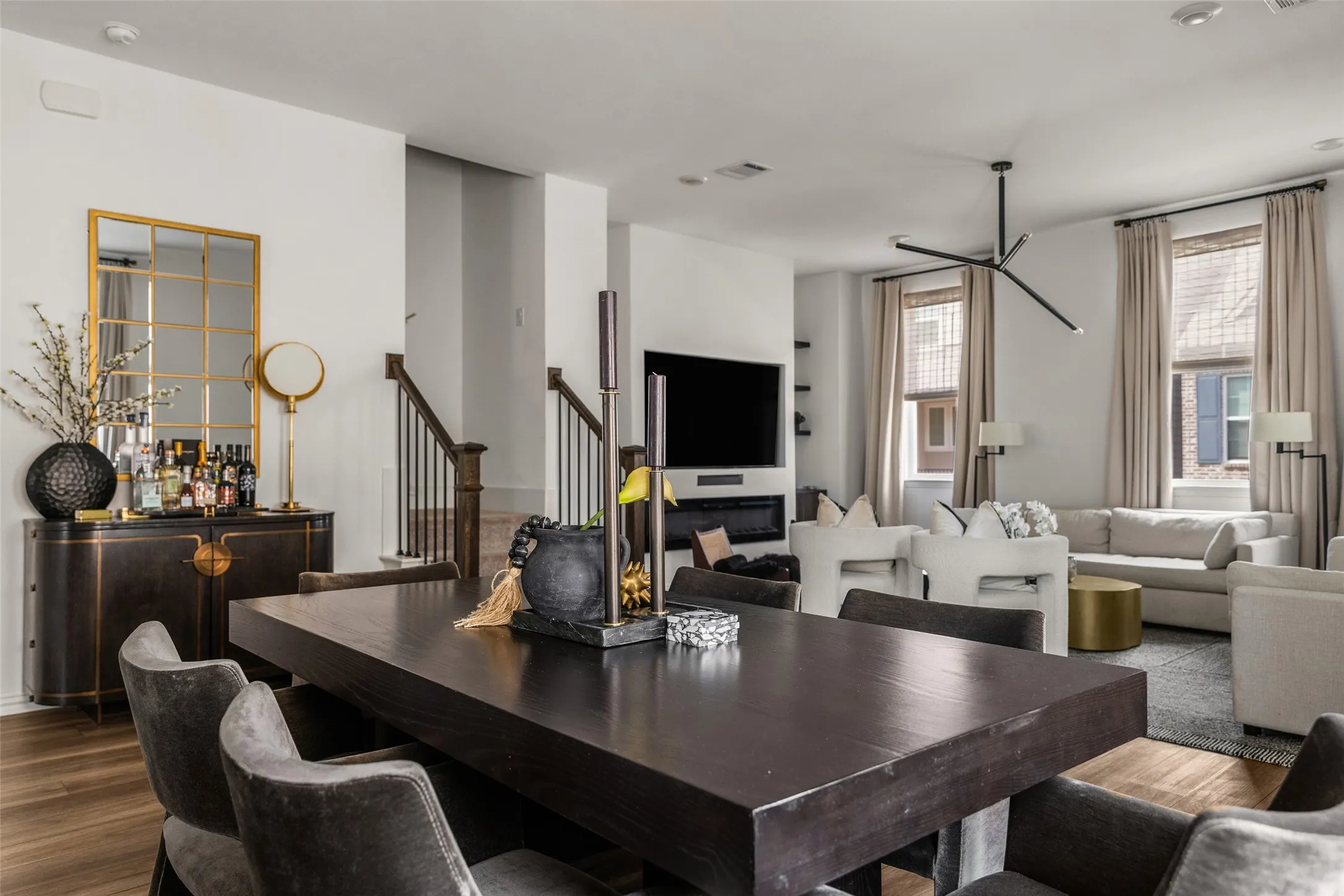 Hardwood-finish flooring, built-in fireplace, contemporary lighting fixture, staircase with wood railing and metal balusters, and multiple windows with blinds and drapery