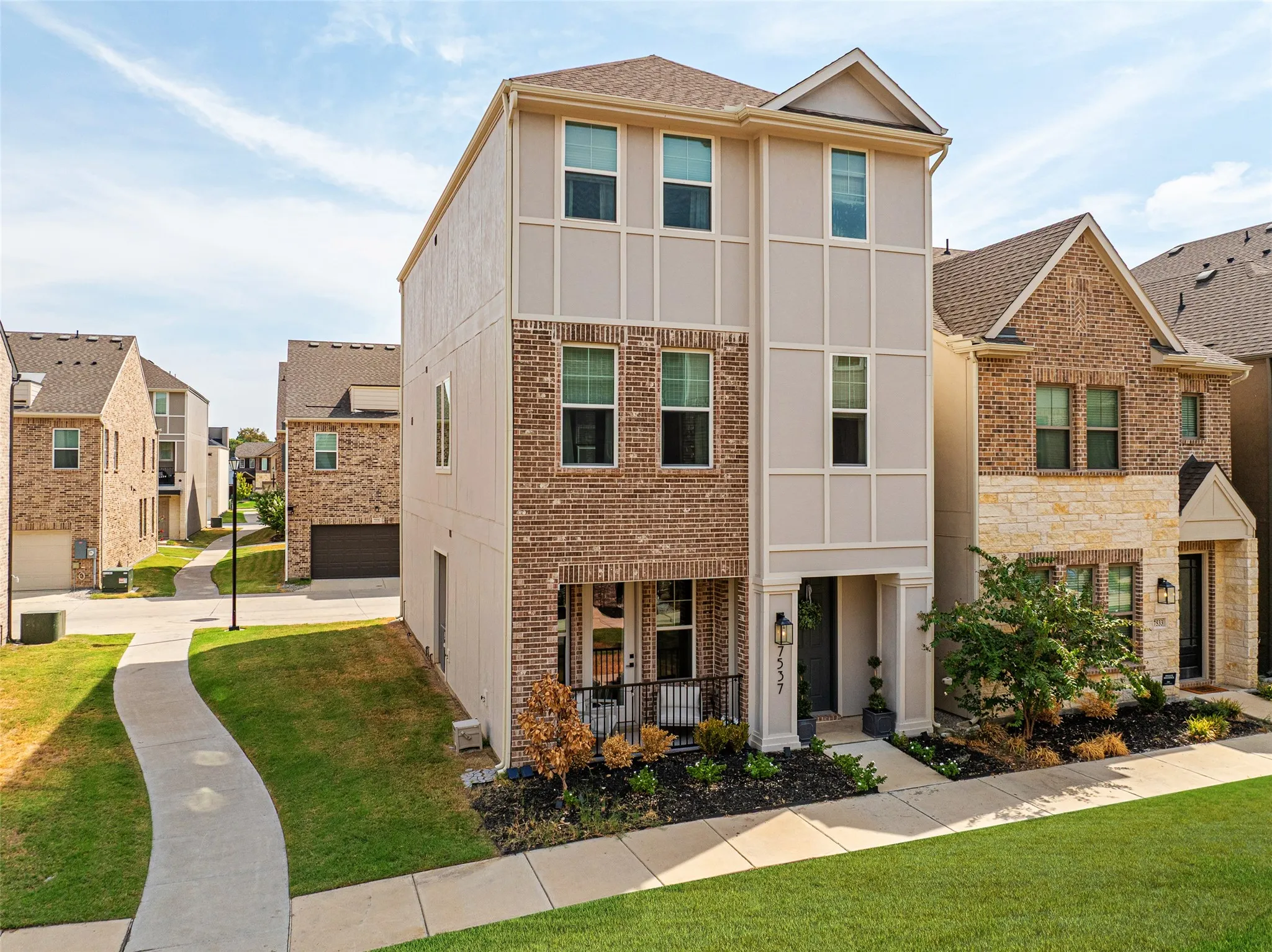 Contemporary three-story property featuring a brick and stucco exterior, prominent front entry with covered porch, and well-maintained landscaping
