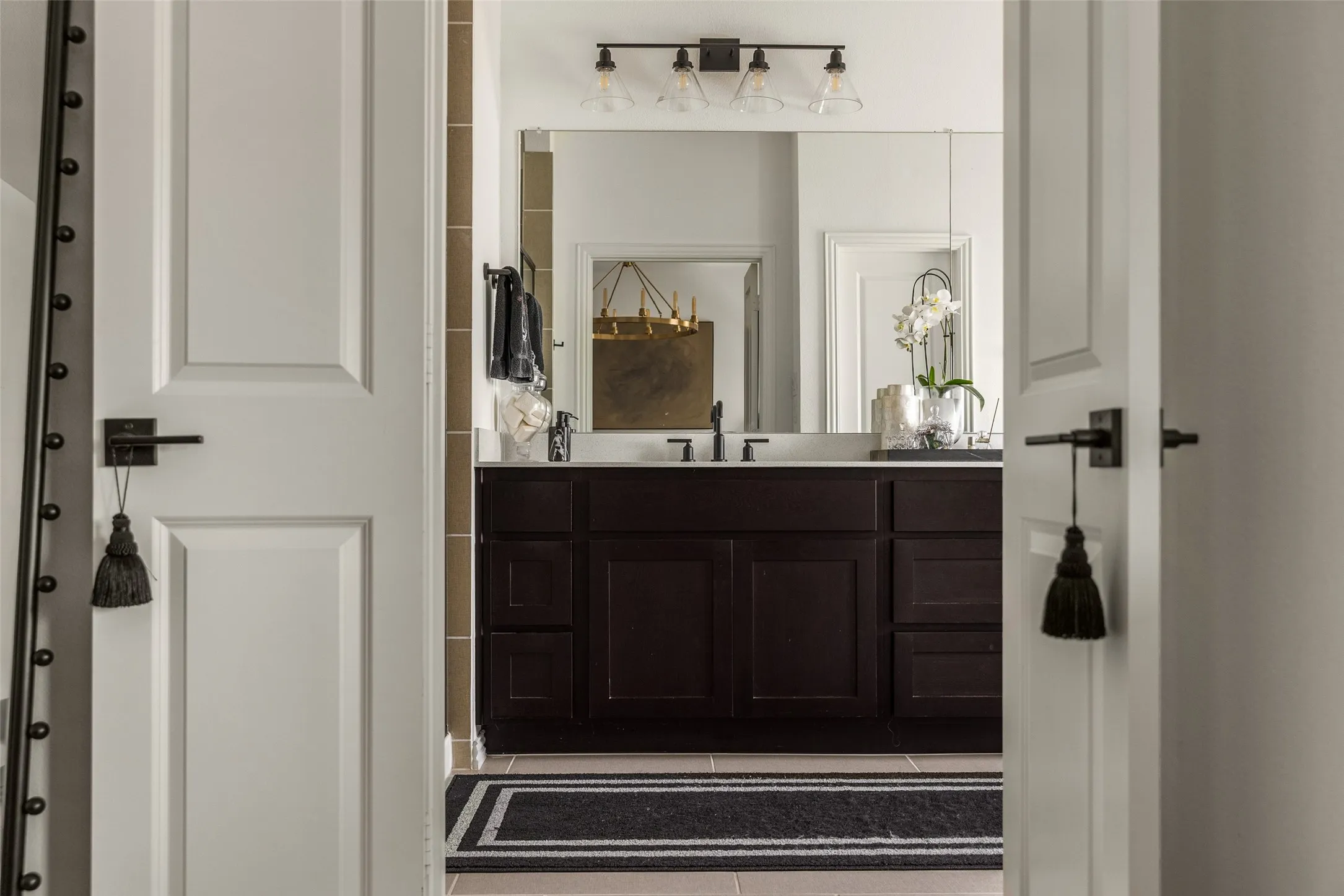 Bathroom vanity featuring dark wood cabinetry, a rectangular mirror, a three-light fixture with clear glass shades, a dark countertop, and matte black fixtures