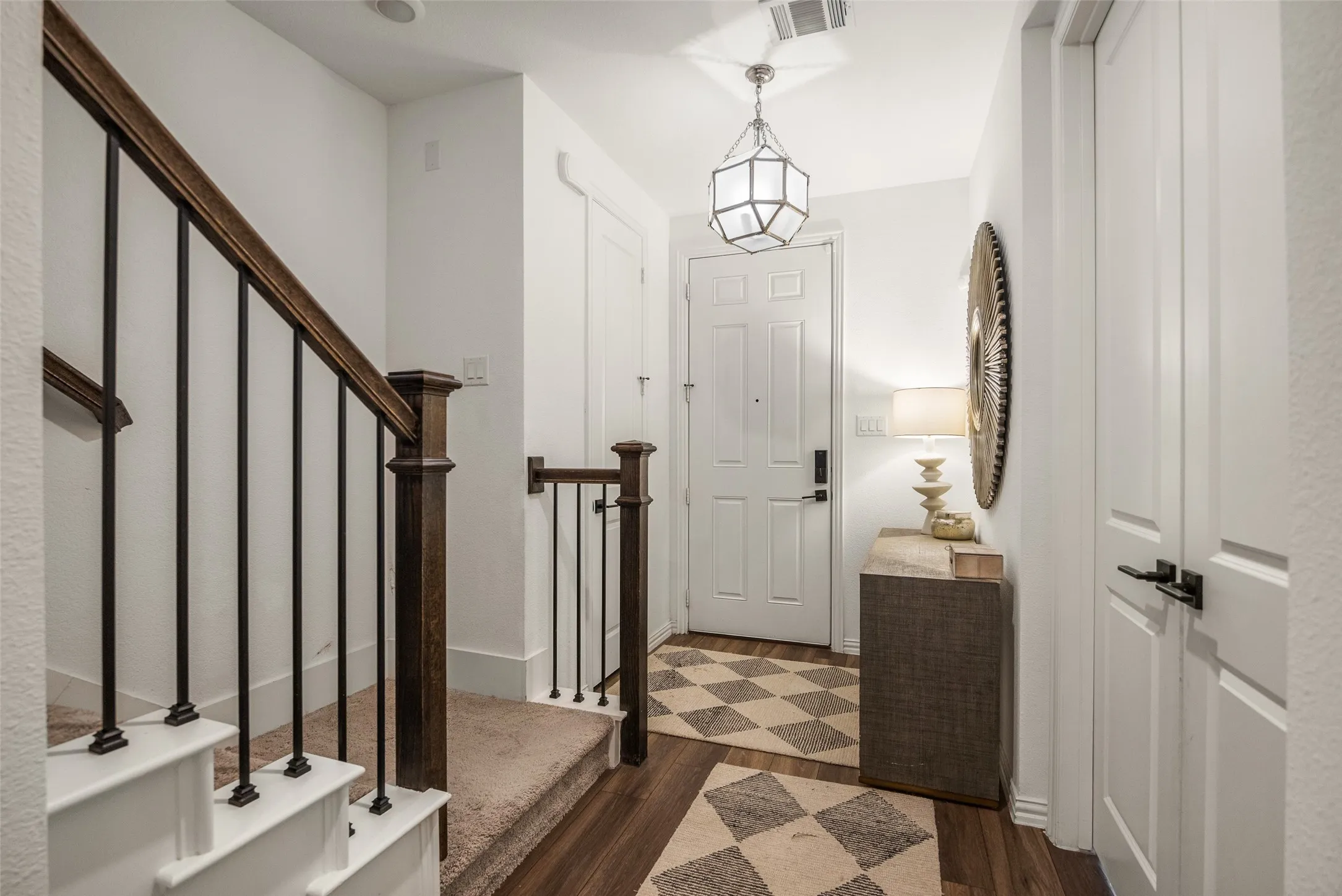 Wood-finish flooring with a geometric area rug, white paneled doors, and a staircase featuring wood newel posts and black metal balusters