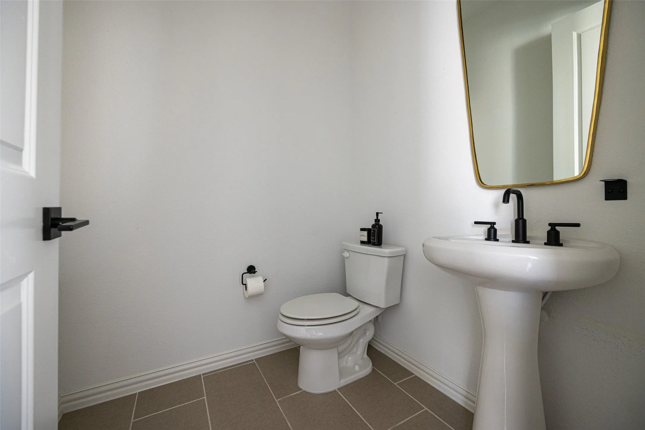 Bright powder room featuring dual pedestal sinks with chrome faucets, a ceramic toilet with elongated bowl, and neutral tile flooring
