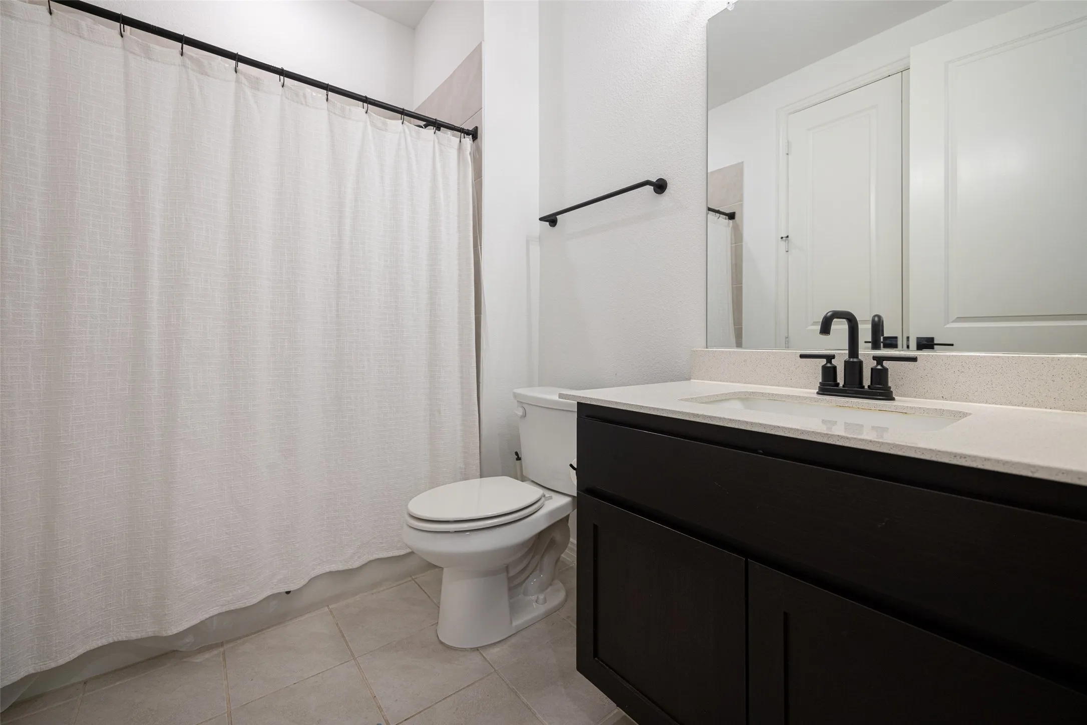 Bathroom featuring a dark wood-finish vanity with a light countertop, black fixtures, and tiled flooring
