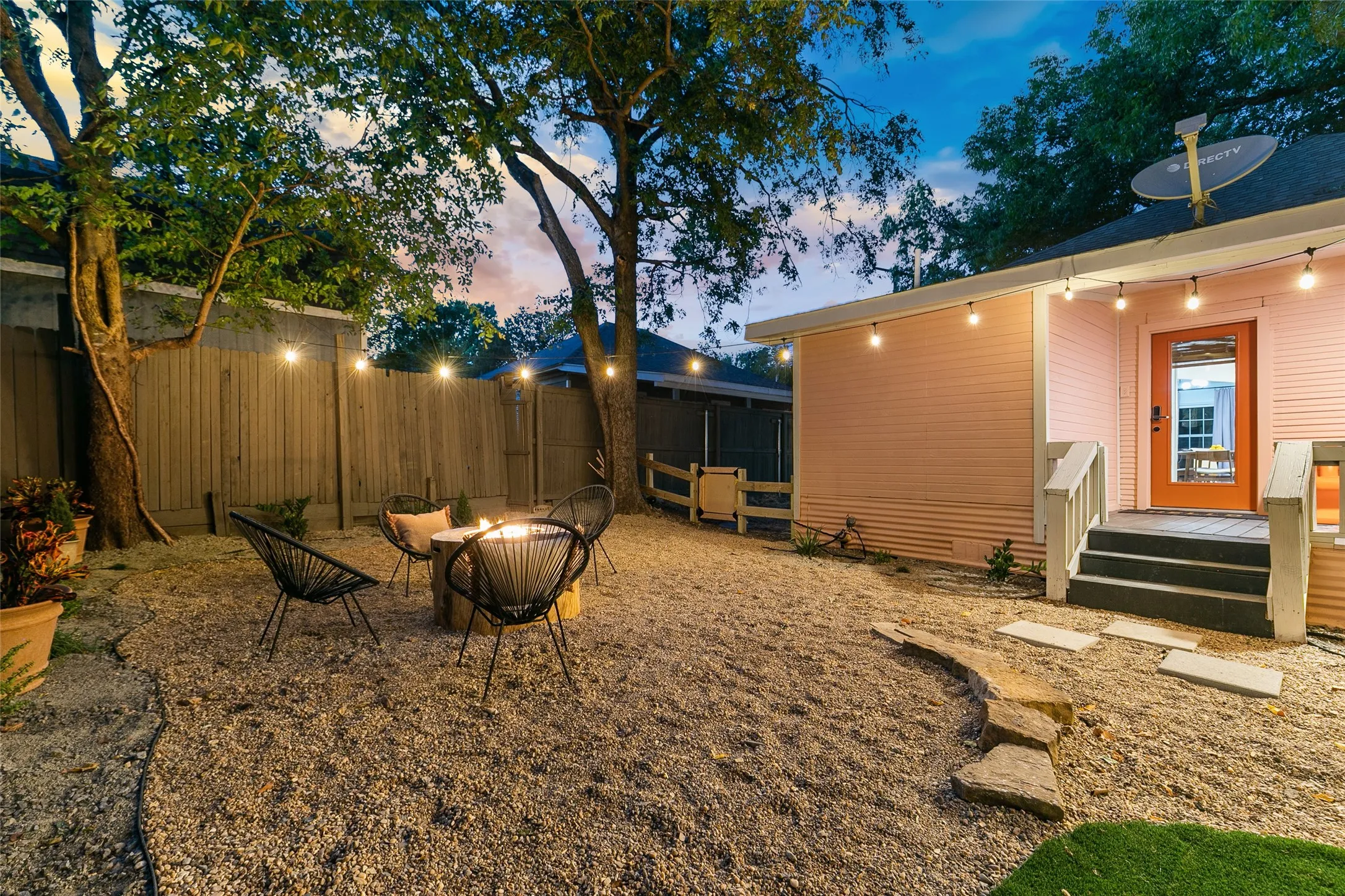 Gravel backyard with a built-in fire pit, string lighting, and wood privacy fencing