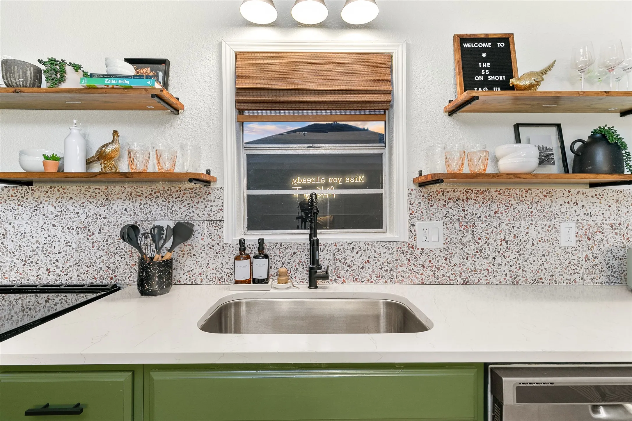 Stainless steel sink with a matte black faucet, light countertop, and green cabinetry