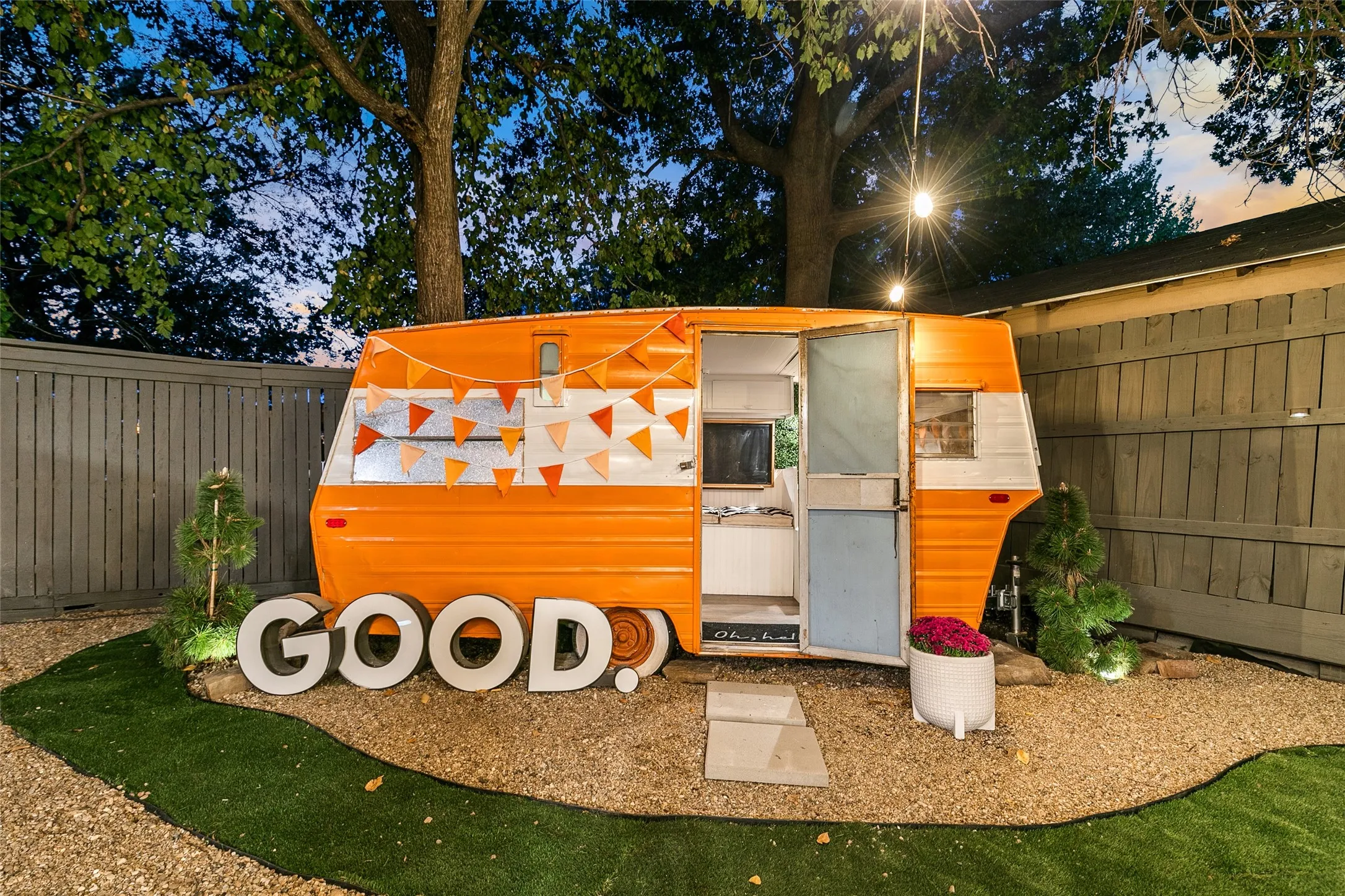 Enclosed private outdoor area featuring a vintage-style trailer, string lighting, and a fenced perimeter