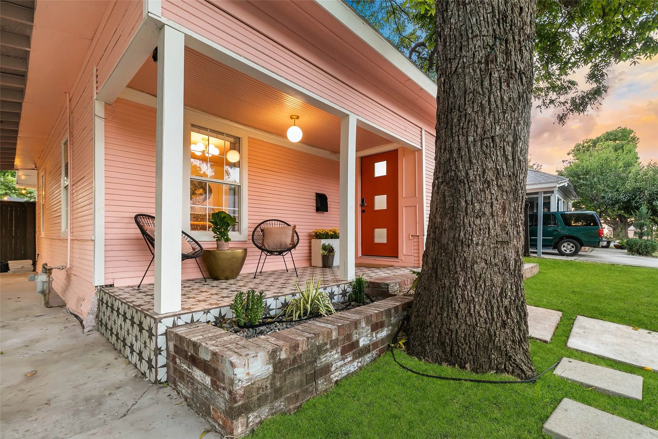 Inviting front porch featuring patterned floor tiles, white support columns, and an orange entry door with square insets