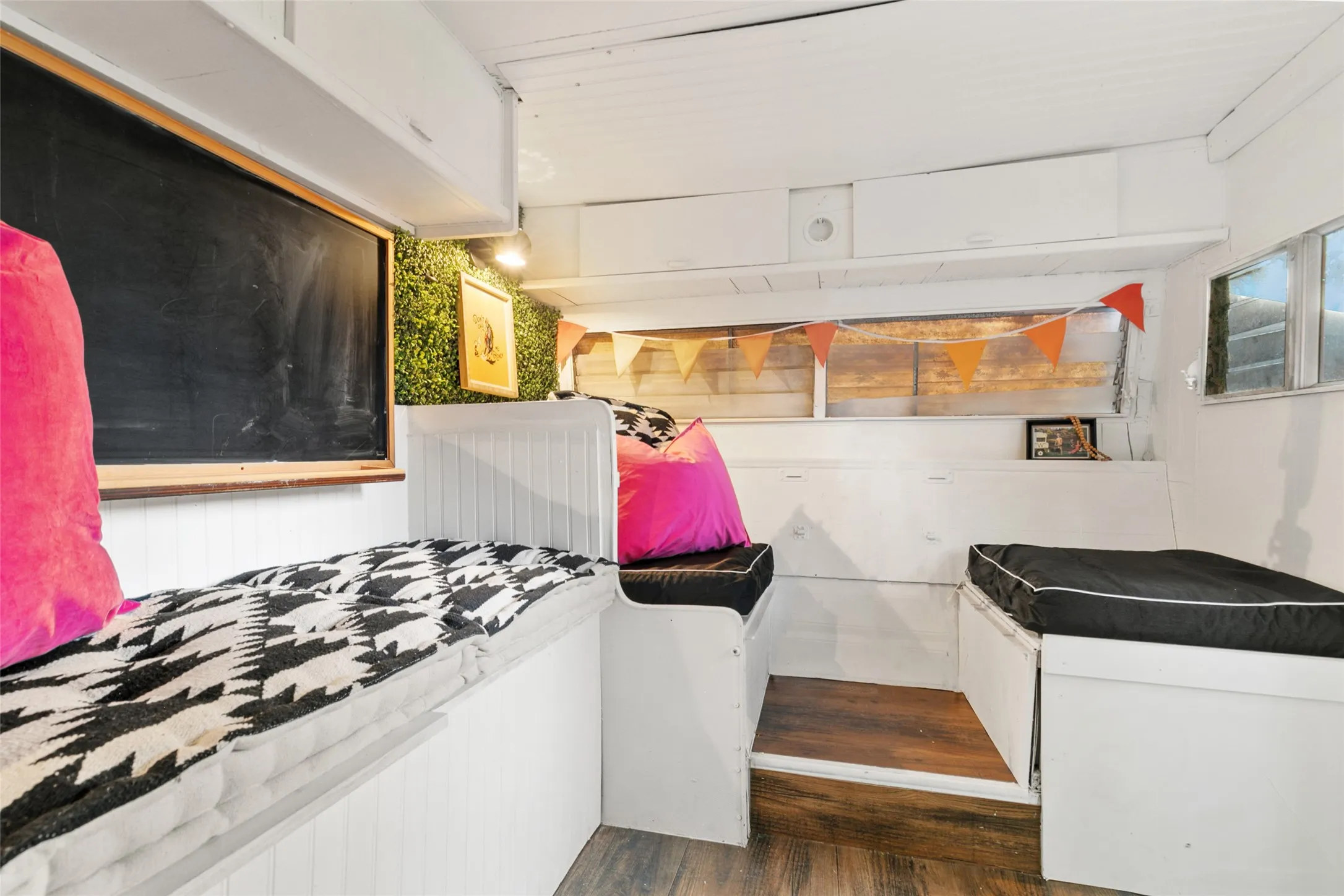 Built-in seating with storage, wood-finish flooring, overhead cabinetry, and a chalkboard feature