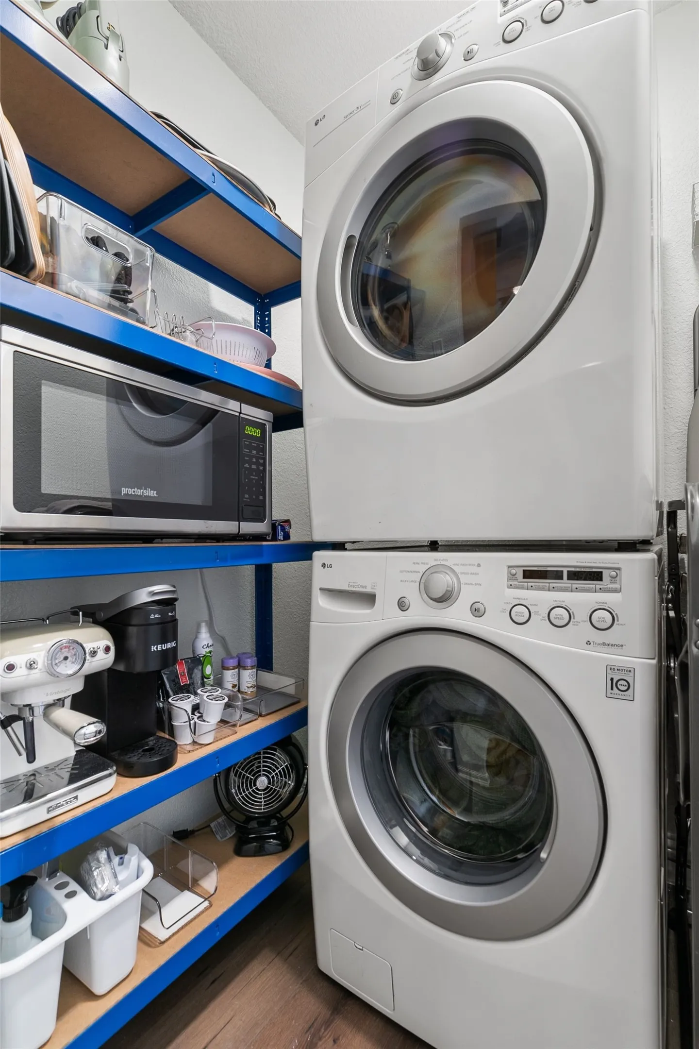Stacked washer and dryer, blue shelving, wood-finish flooring