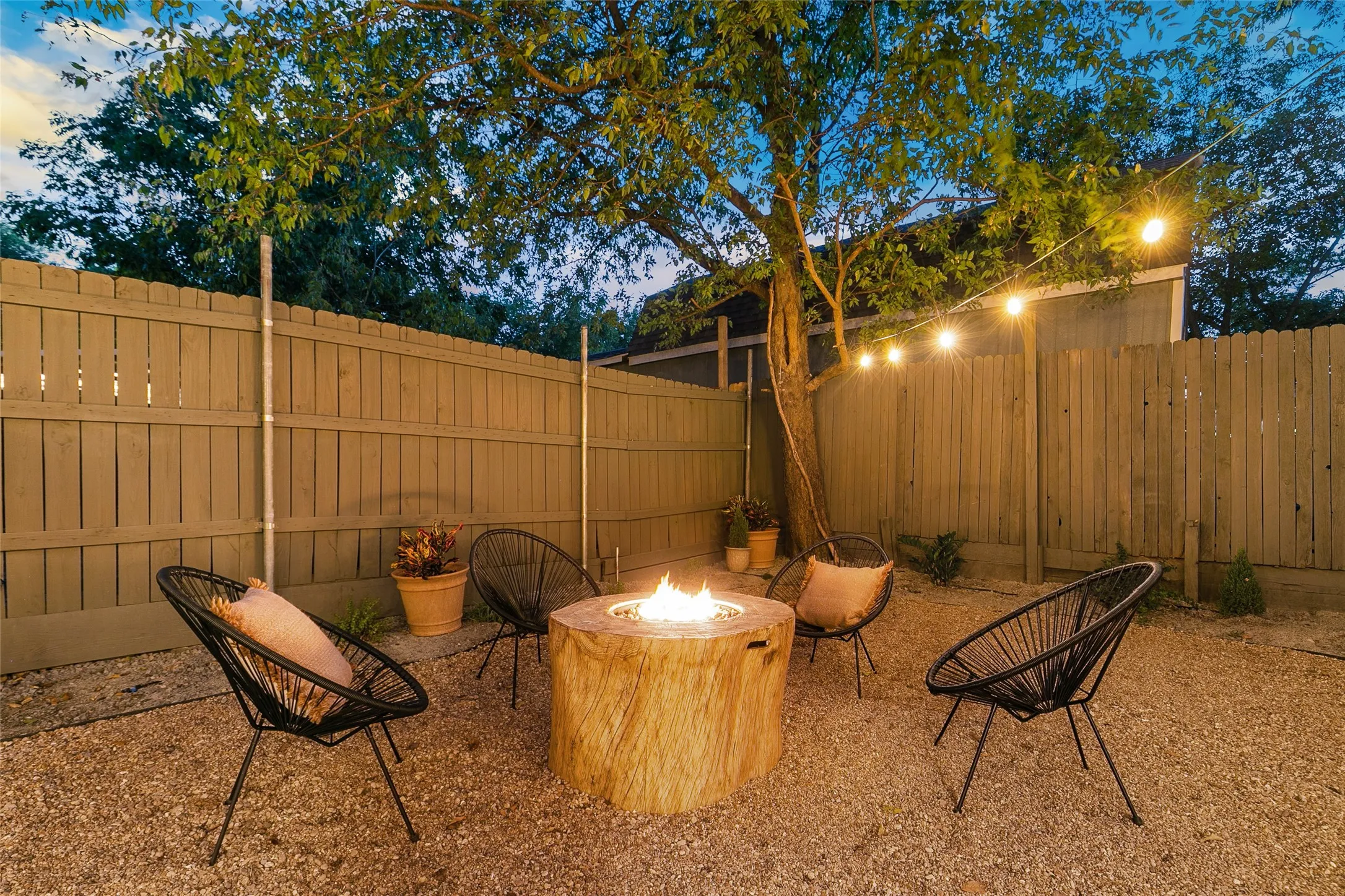 Gravel patio featuring a built-in fire pit, privacy fencing, and mature trees