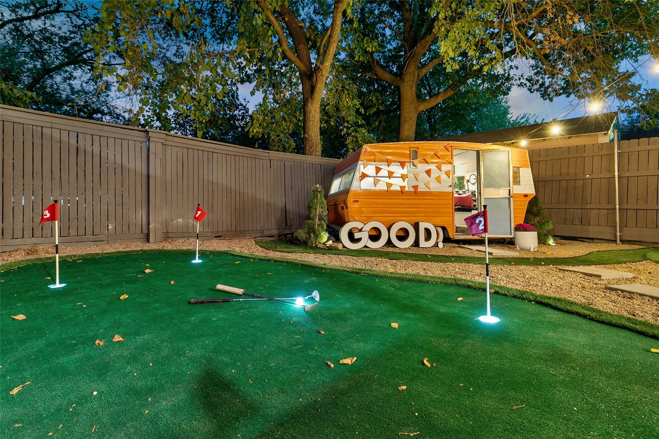 Backyard putting green with multiple holes, gravel pathways, a privacy fence, and a unique wood-sided structure