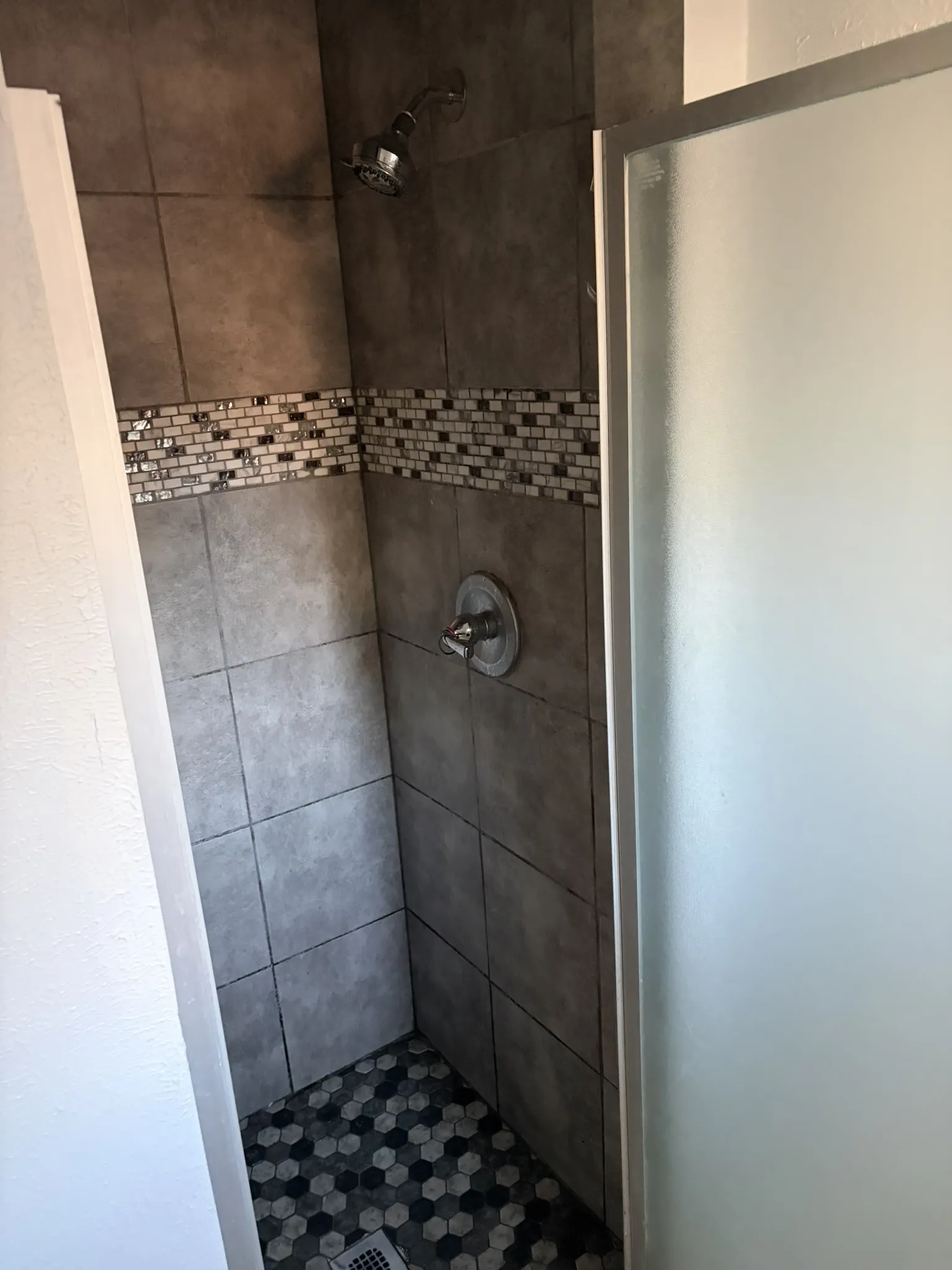 Tiled shower enclosure with a mosaic accent band and hexagonal floor tiles