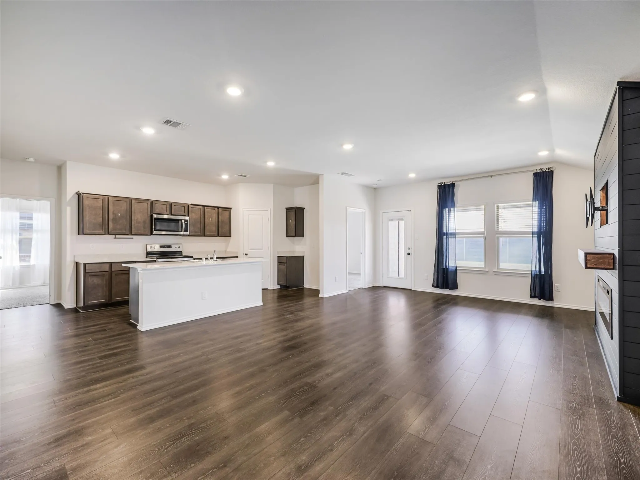 Open-concept living space with wood-finish flooring, a kitchen island, recessed lighting, and a built-in fireplace