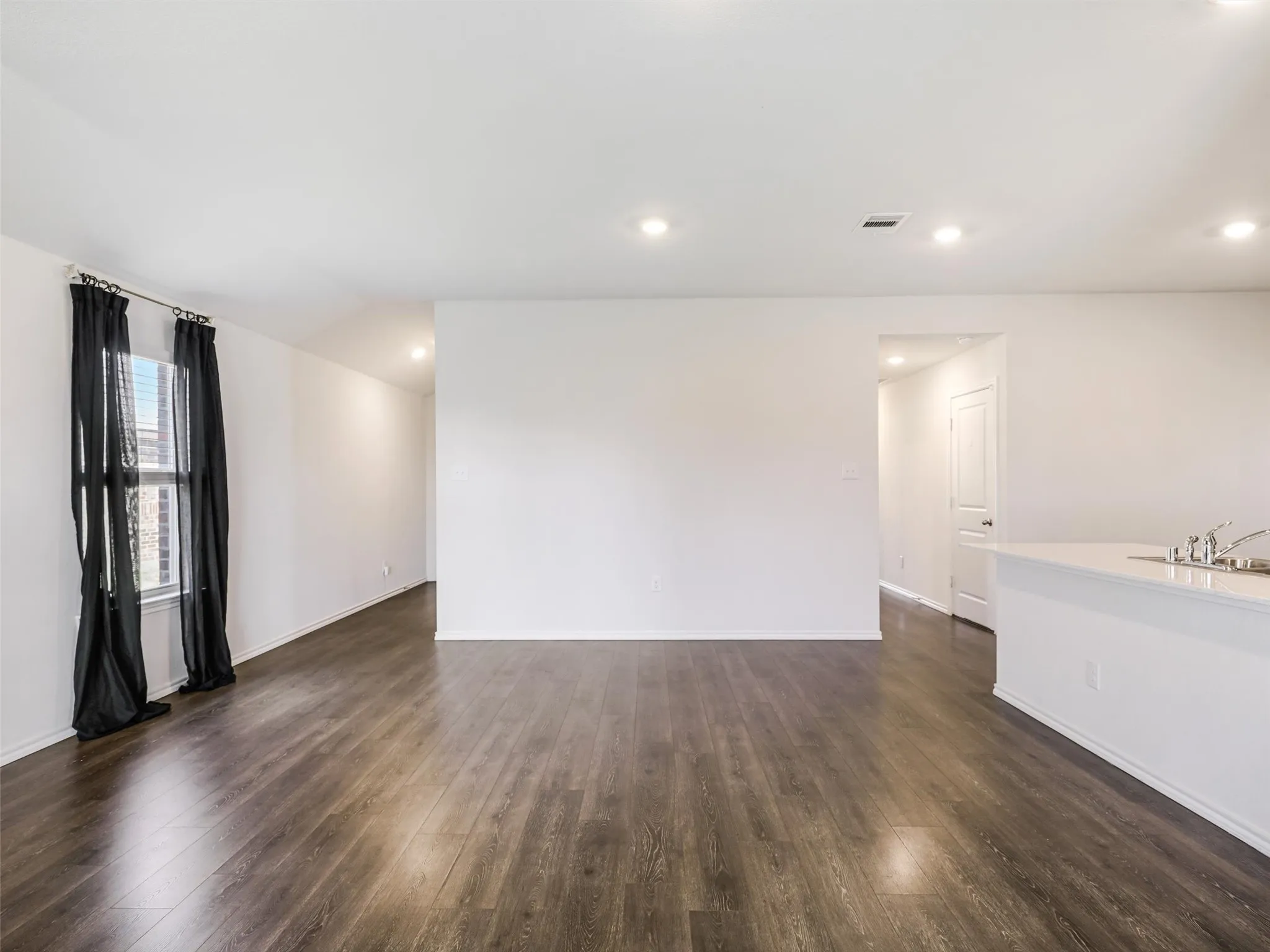 Wood-finish flooring throughout, recessed ceiling lighting, a window with vertical mullions, and a kitchen counter with an integrated sink