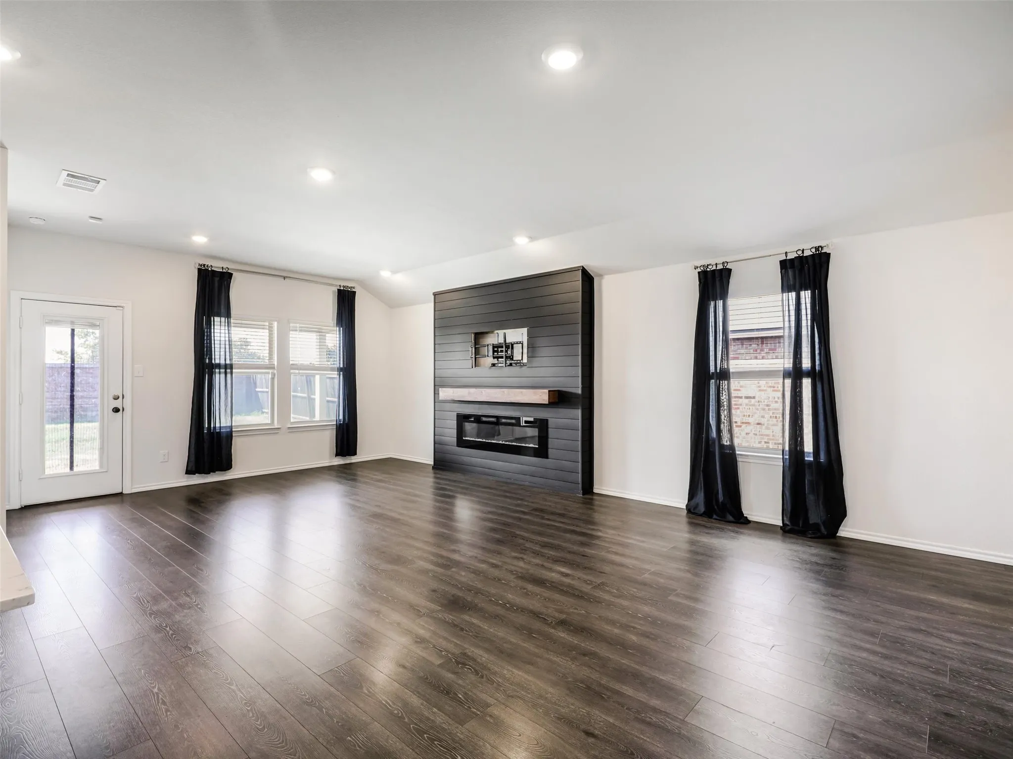 Spacious room featuring wood-finish flooring, recessed lighting, and a modern fireplace with a wood mantle