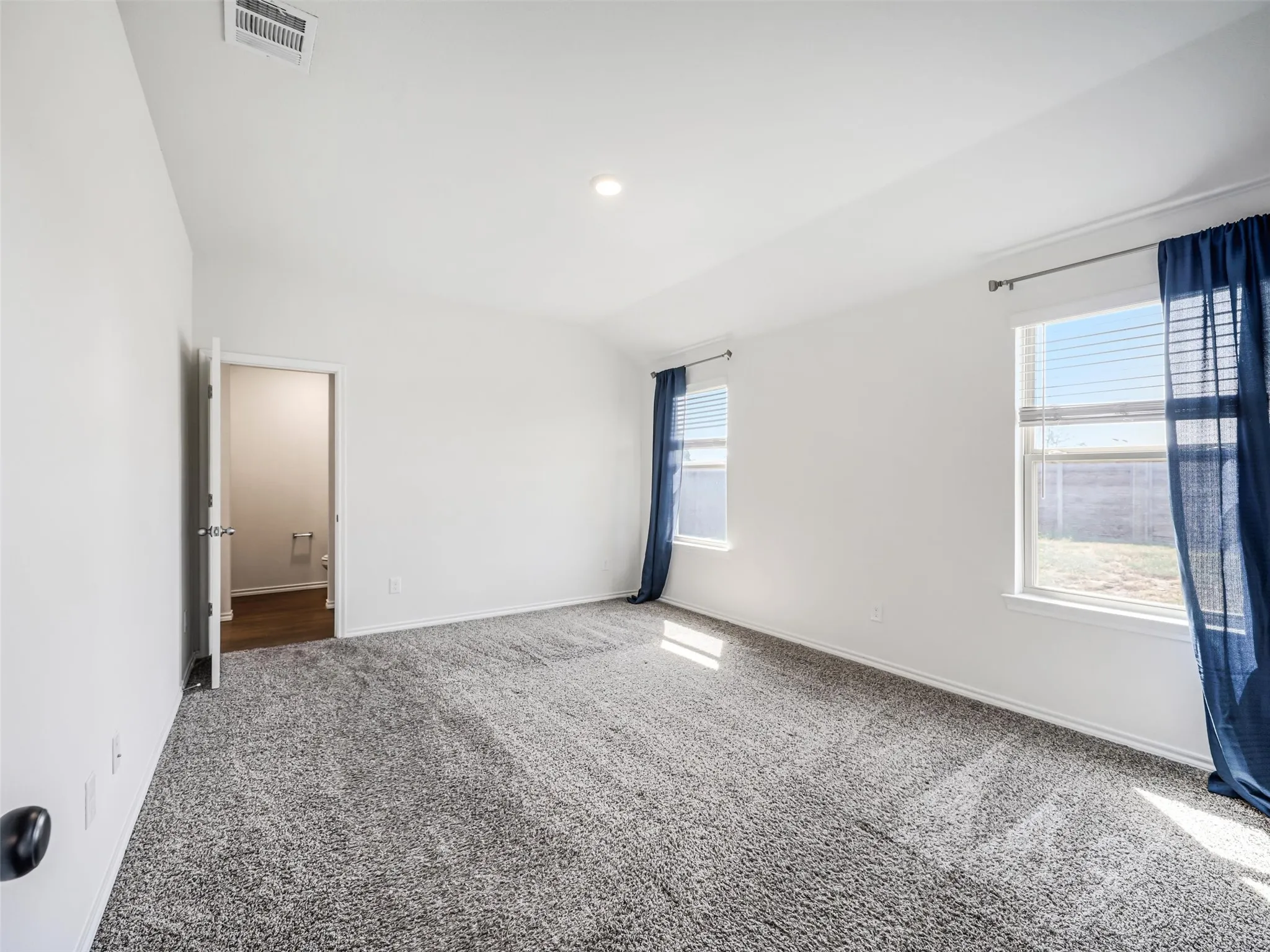 Vaulted ceiling, two windows, recessed lighting, gray carpet, and white walls