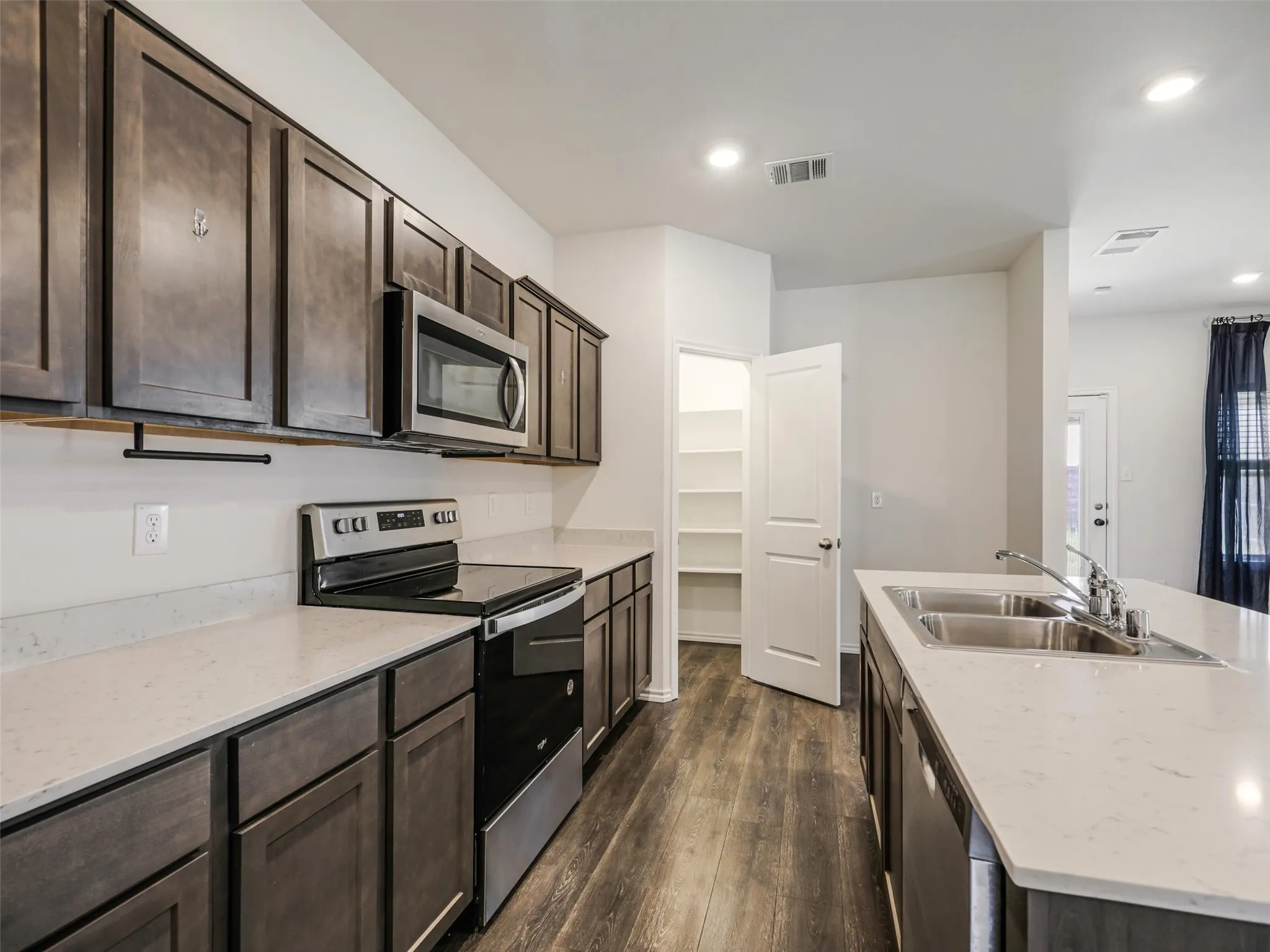 Modern kitchen featuring stainless steel appliances, wood-finish flooring, light quartz countertops, dark cabinetry with ample storage, and a generous island with undermount sink