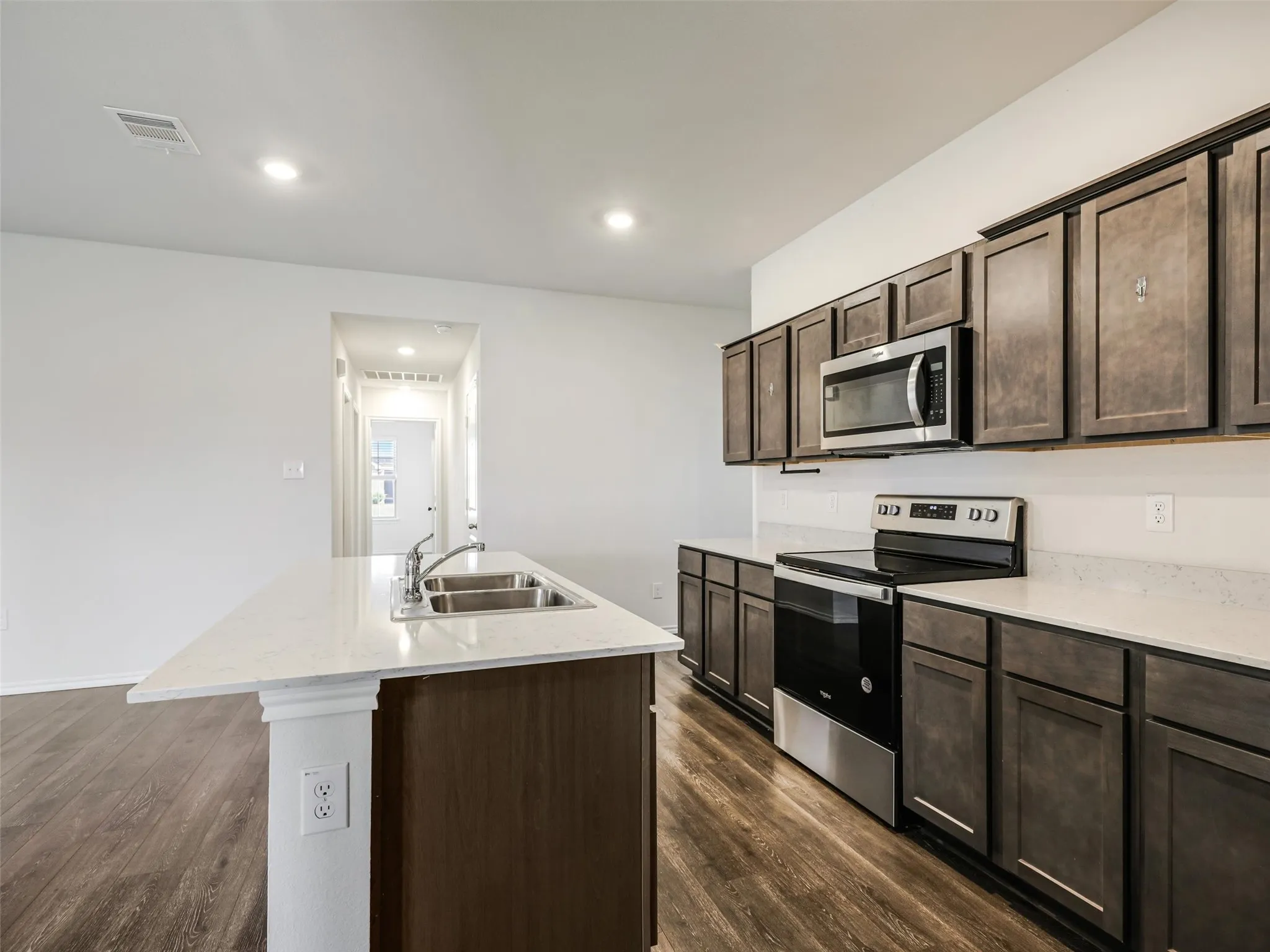 Kitchen featuring an island with double basin sink, dark wood-finish cabinetry, light-toned countertops, stainless steel appliances, and wood-finish flooring