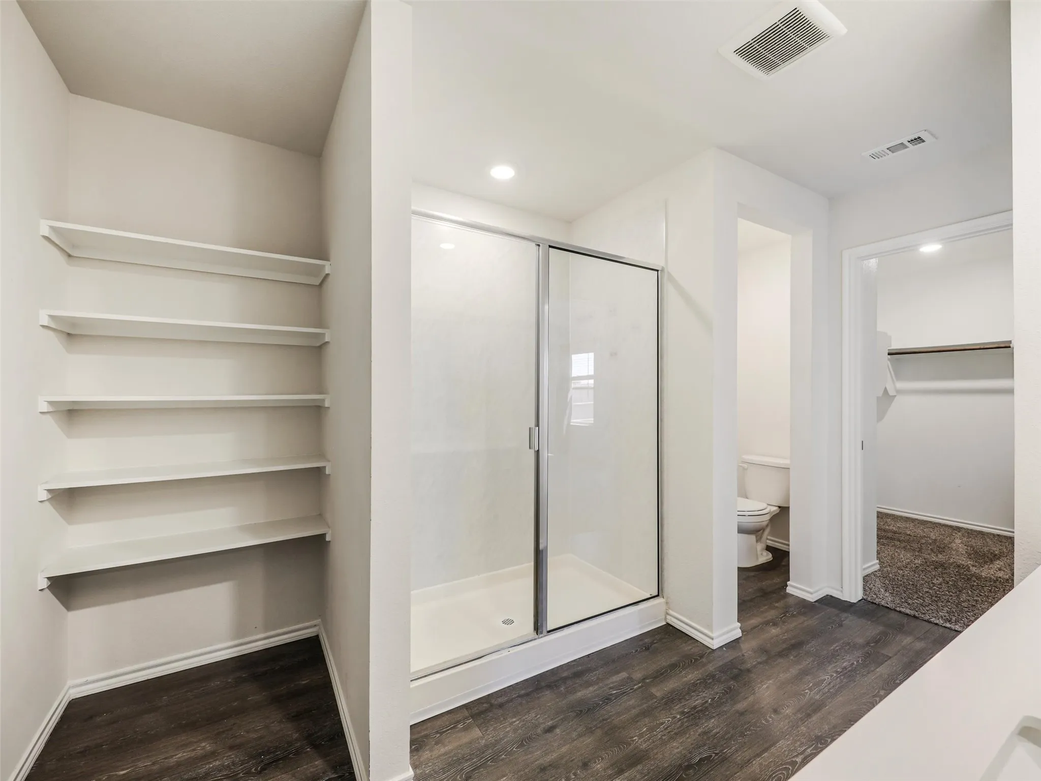 Spacious walk-in shower with a glass enclosure, built-in shelving, wood-finish flooring, recessed lighting, and a neutral color palette