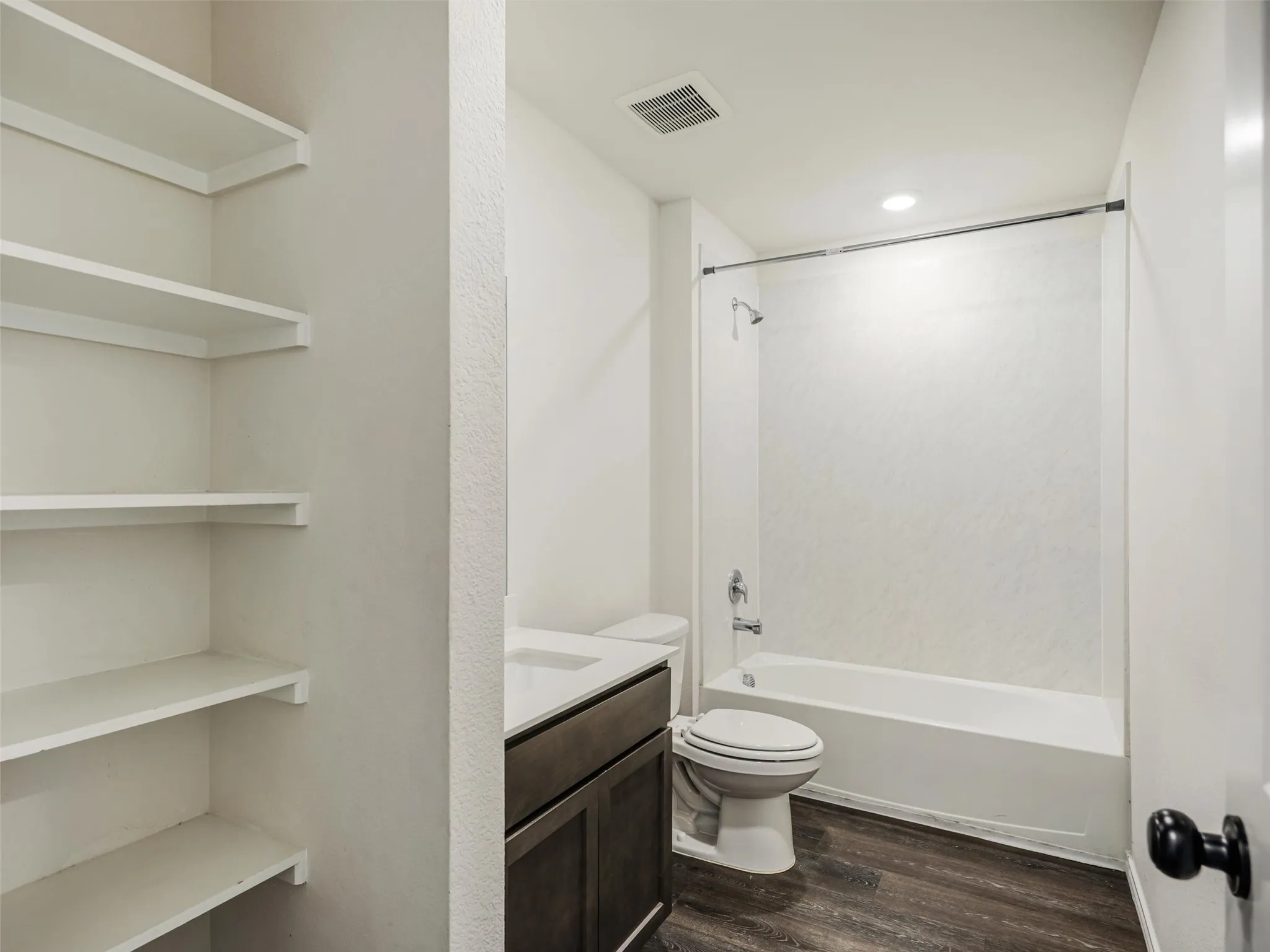 Full bathroom featuring a white tub/shower combination, dark wood-finish vanity, integrated sink, and built-in shelving
