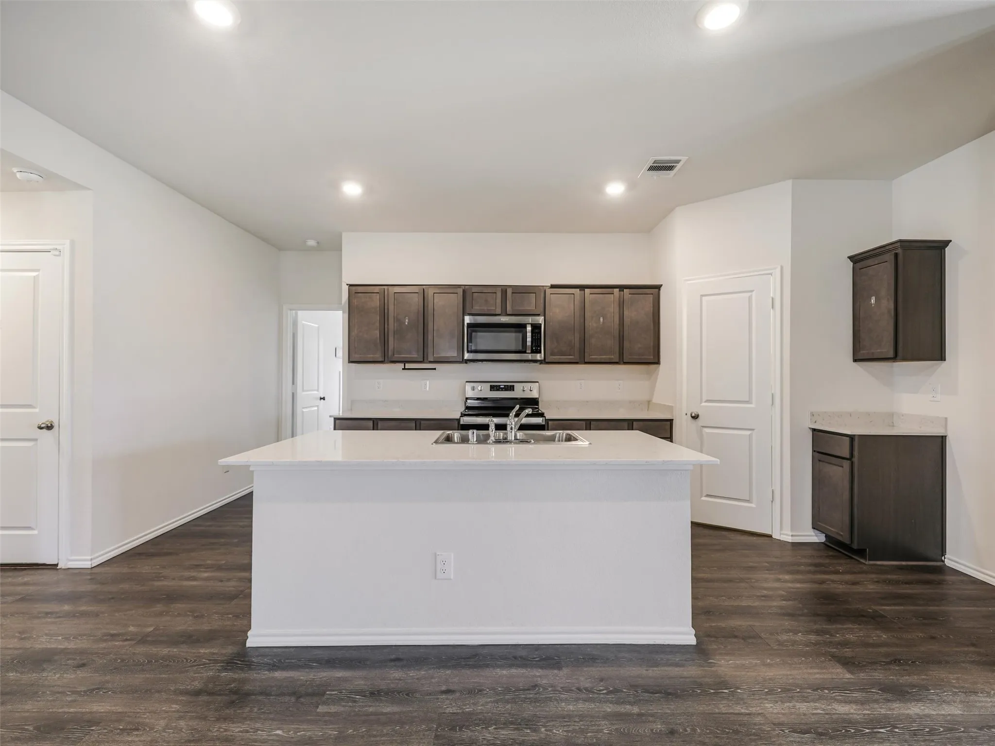 Kitchen featuring a central island with an integrated sink, dark wood-finish cabinetry, stainless steel appliances, and light-colored countertops