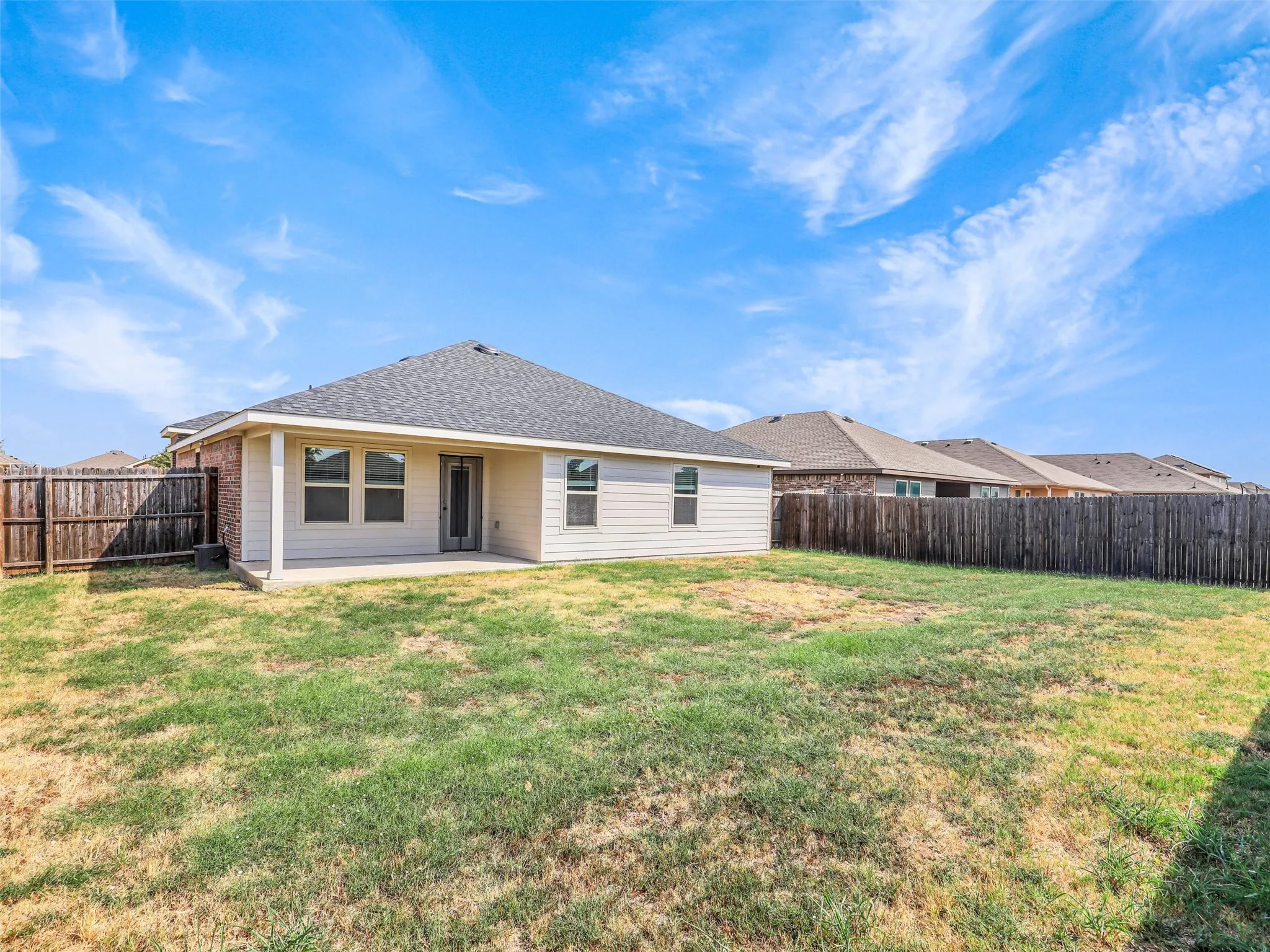 Expansive backyard featuring a concrete patio, wood fencing, and a neutral-toned exterior with multiple windows