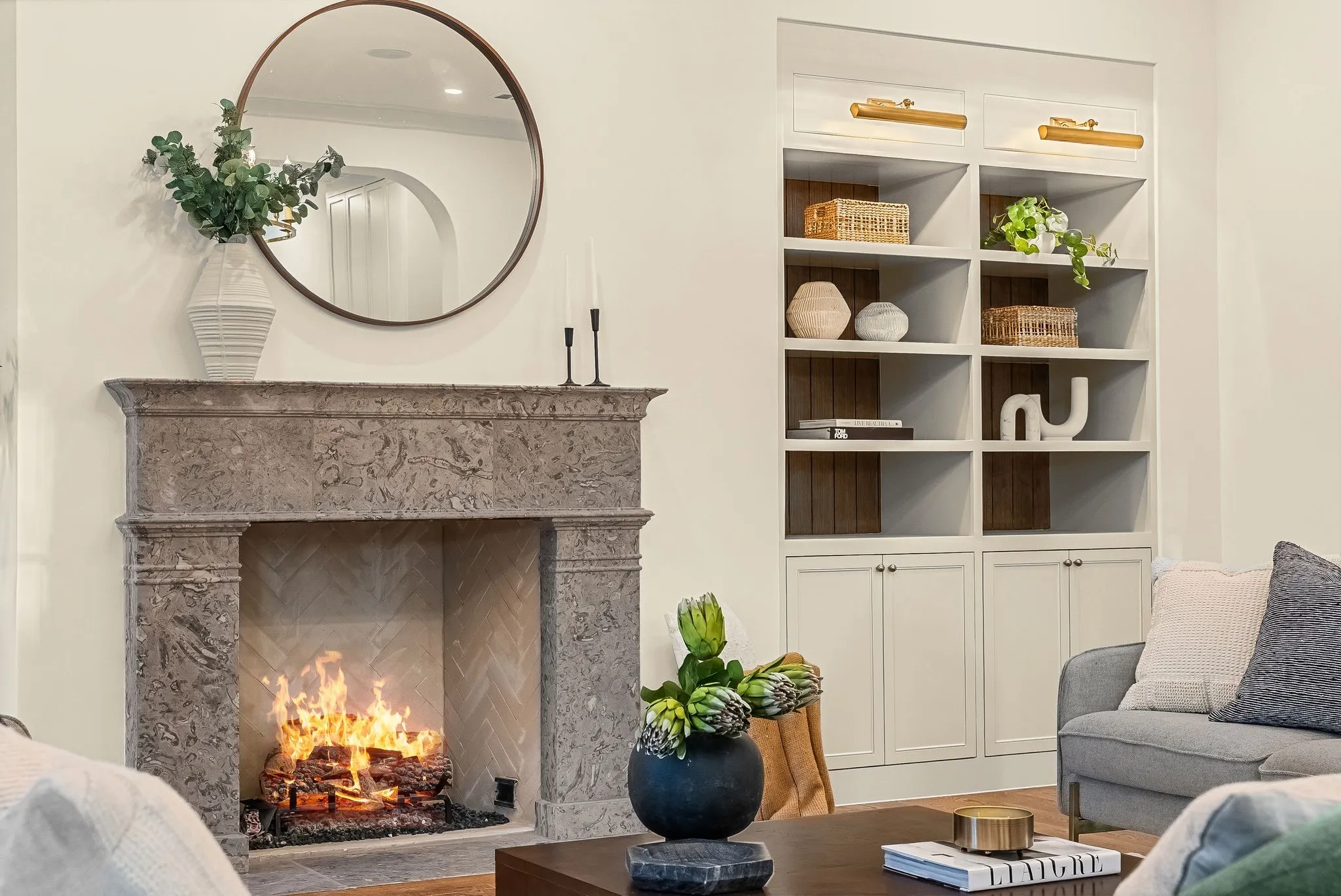 Stone-clad fireplace with a herringbone-patterned firebox, accompanied by built-in shelving featuring integrated lighting and lower cabinetry