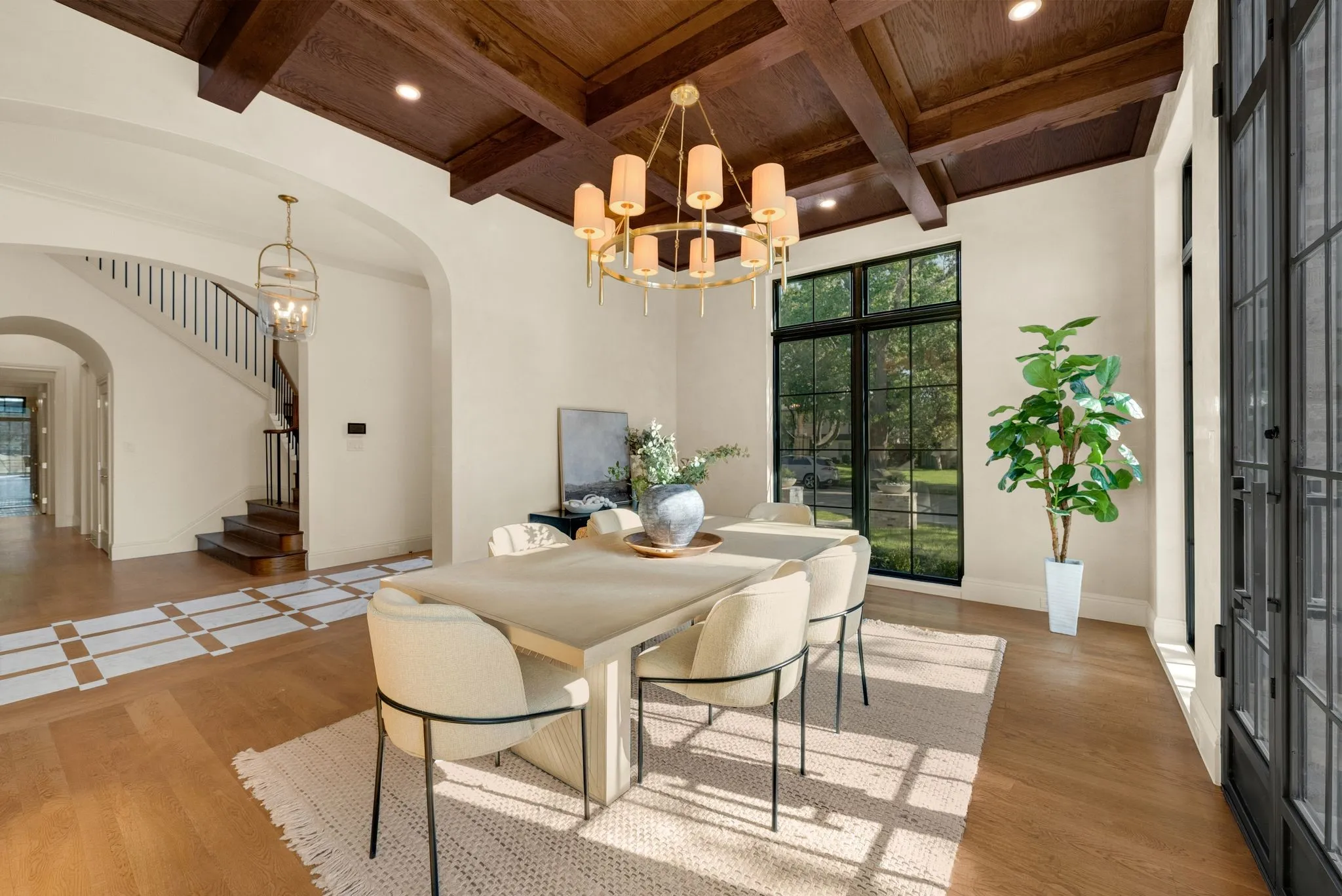 Wood-finish flooring with decorative inlays, coffered wood ceiling, arched doorways, a large multi-pane window, and a built-in staircase with dark banisters