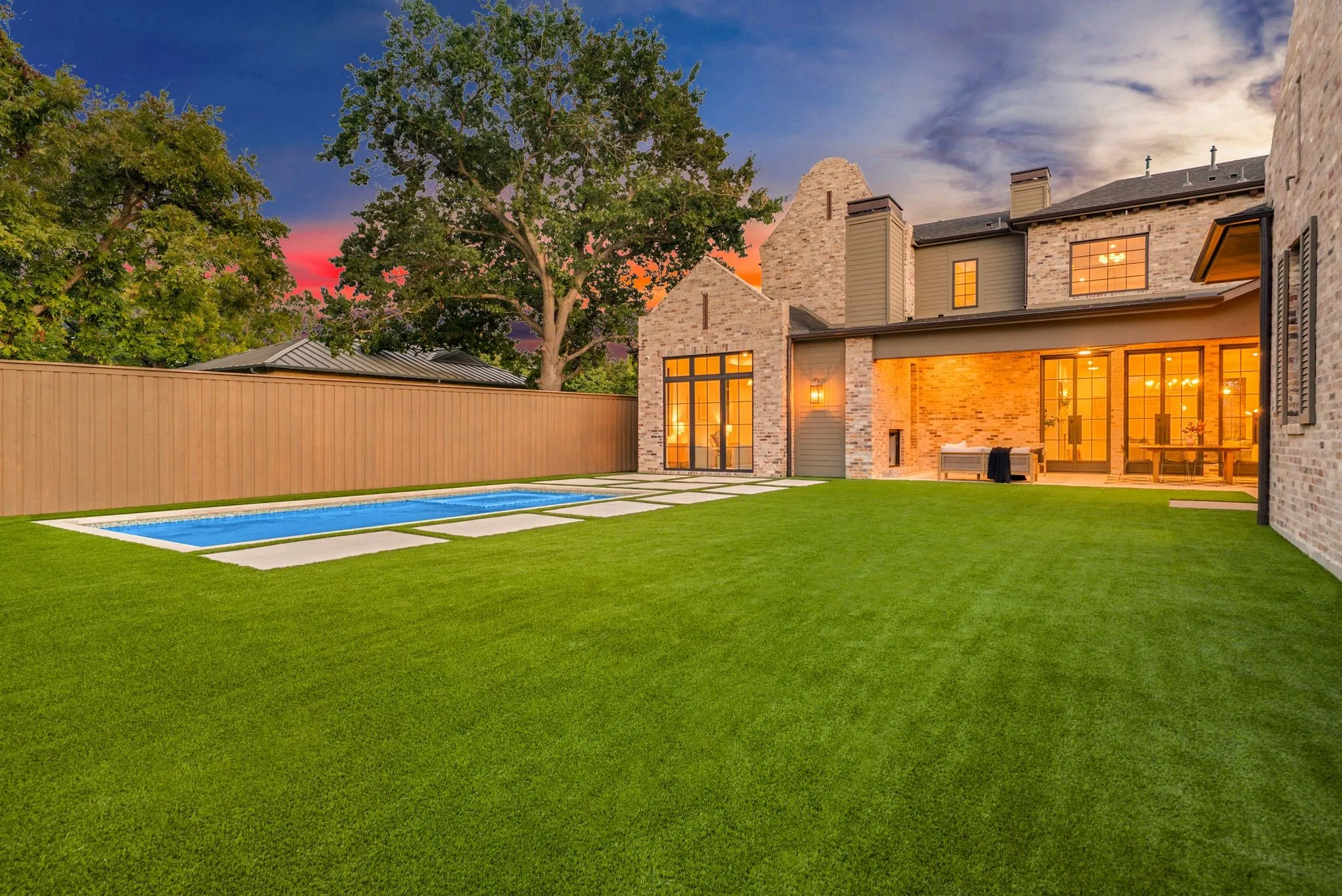 Expansive backyard featuring a rectangular swimming pool with surrounding hardscaping, a manicured lawn, and a wood privacy fence