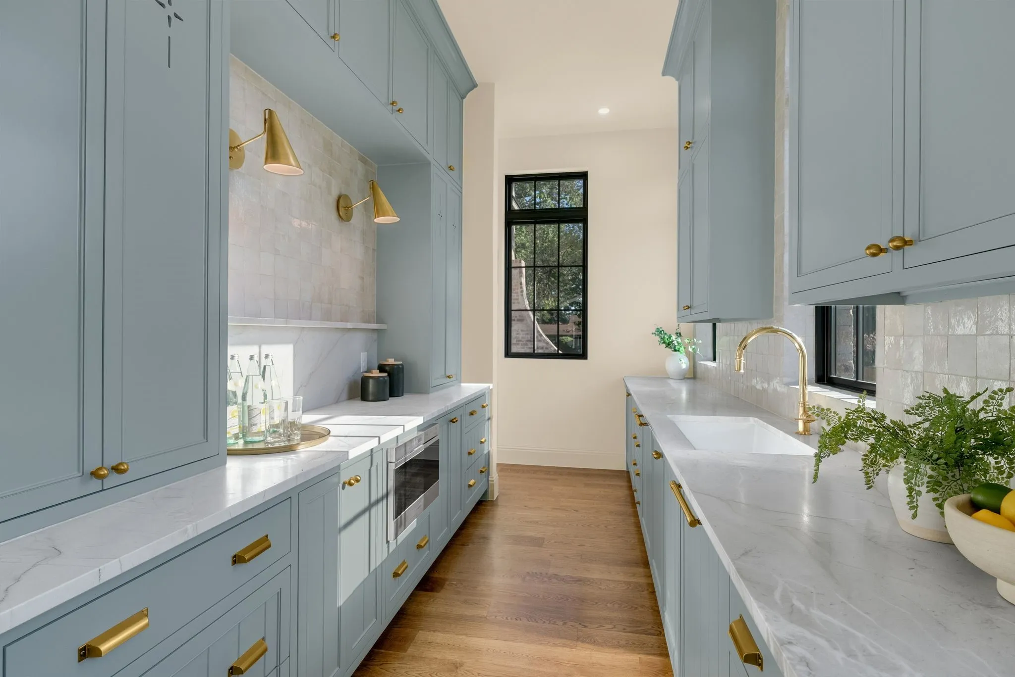 Extensive built-in cabinetry with brass hardware, undermount sink with a brass faucet, integrated microwave, and white countertops