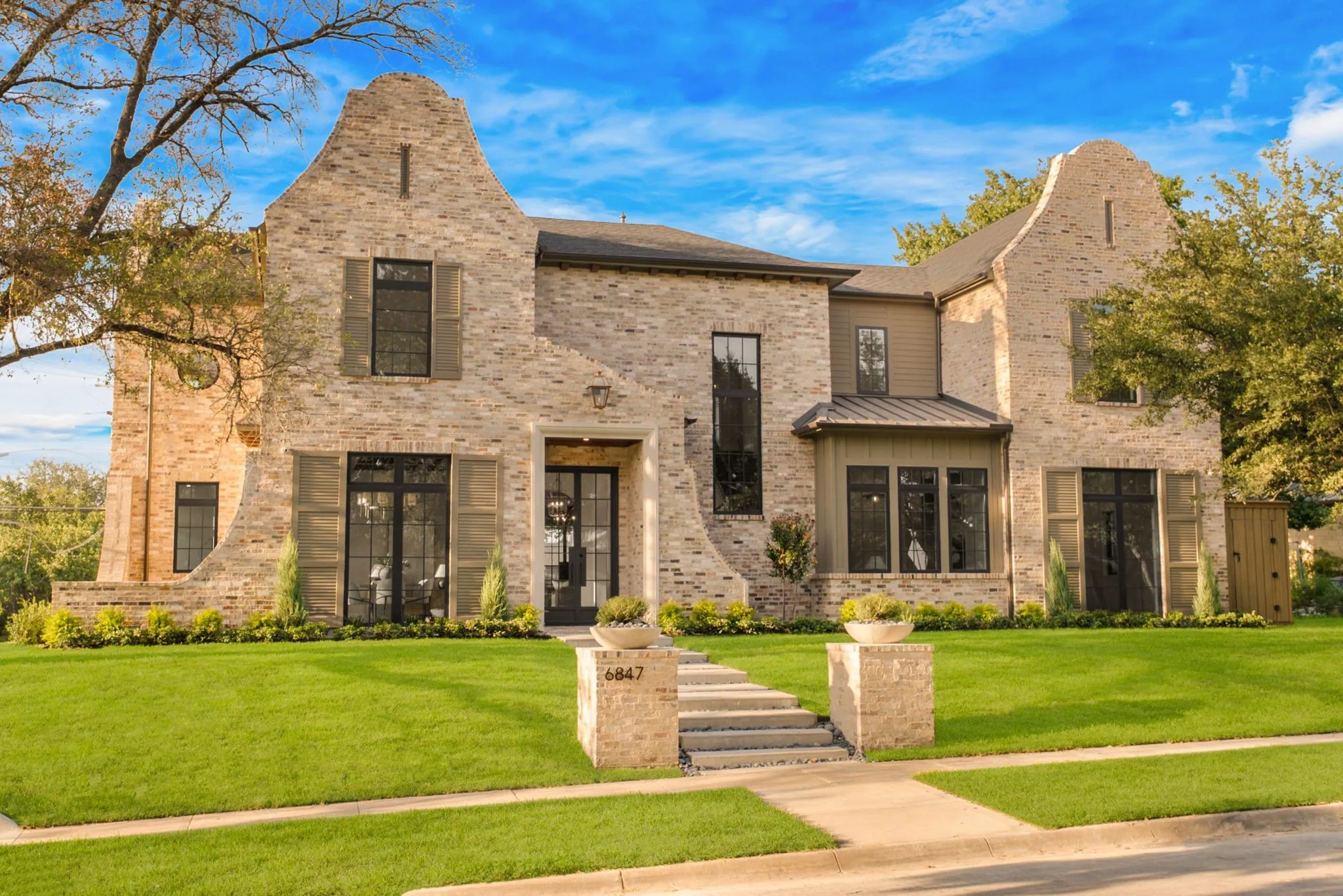 Brick and stone exterior with architectural gables, manicured lawn, stone-clad entrance pillars, and a multi-pane front door