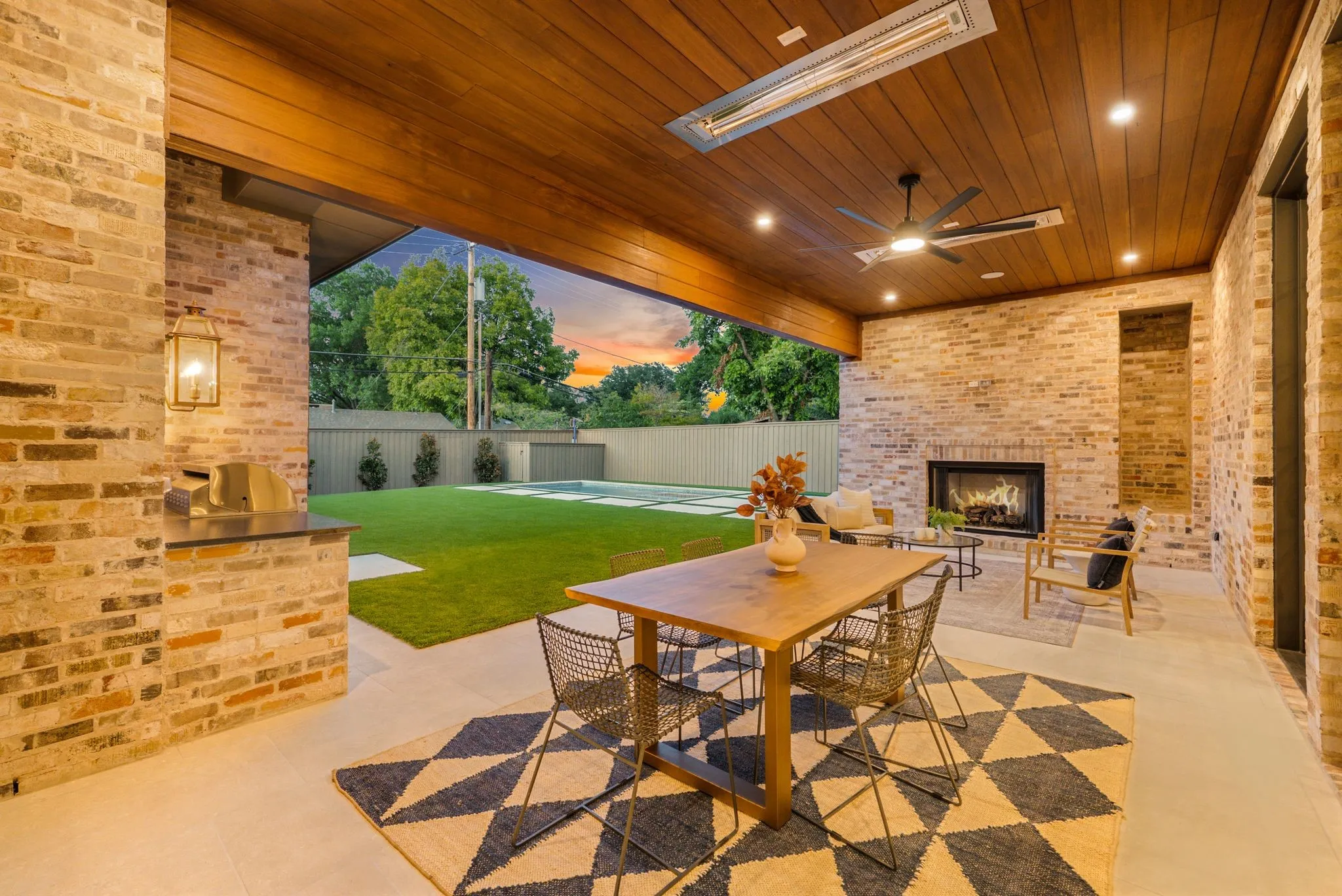 Covered patio with a wood-finish ceiling, built-in brick fireplace, integrated outdoor kitchen, and recessed lighting
