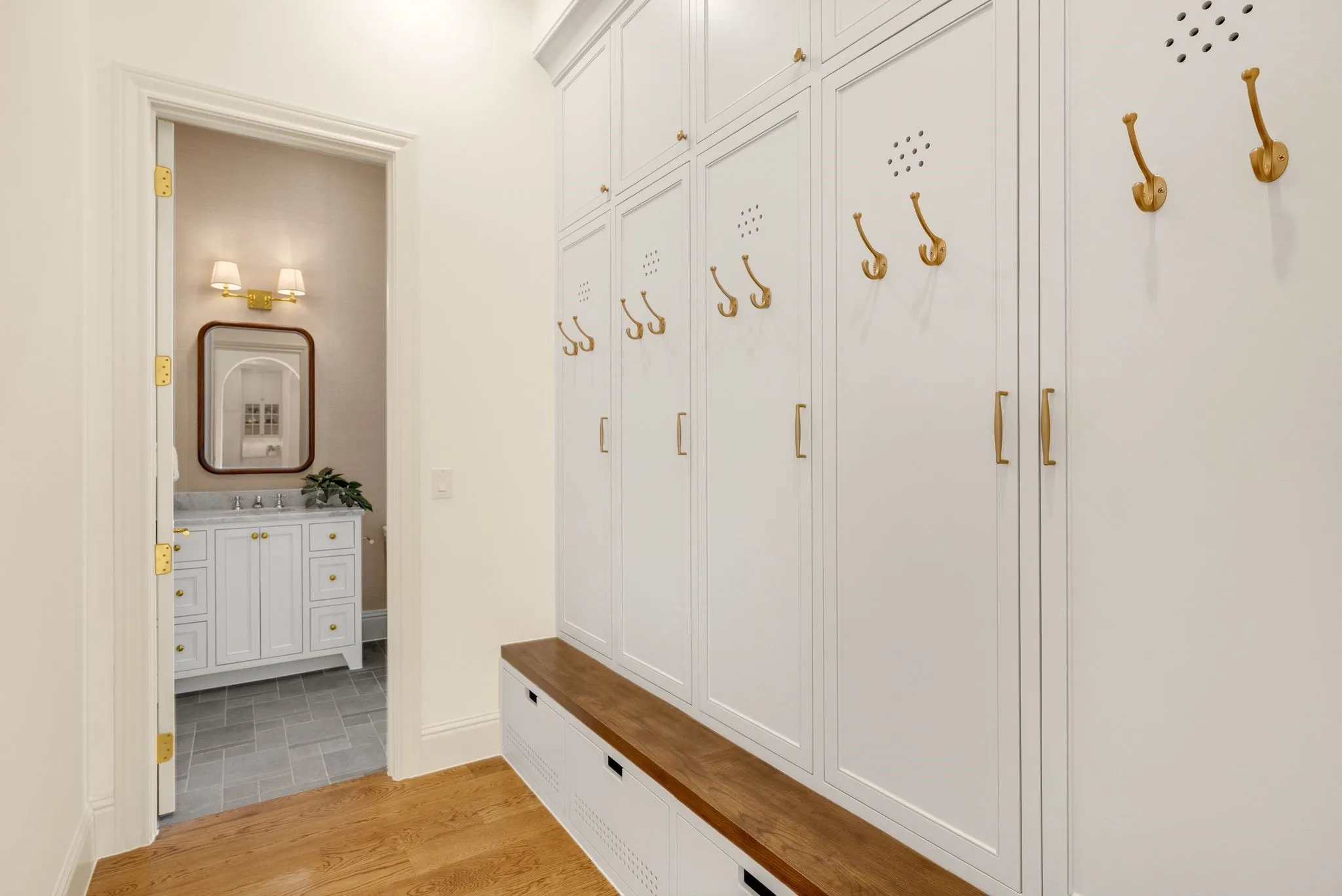 Hardwood-finish flooring, built-in white cabinetry with gold hardware, wood-finish bench, and a separate room with a vanity