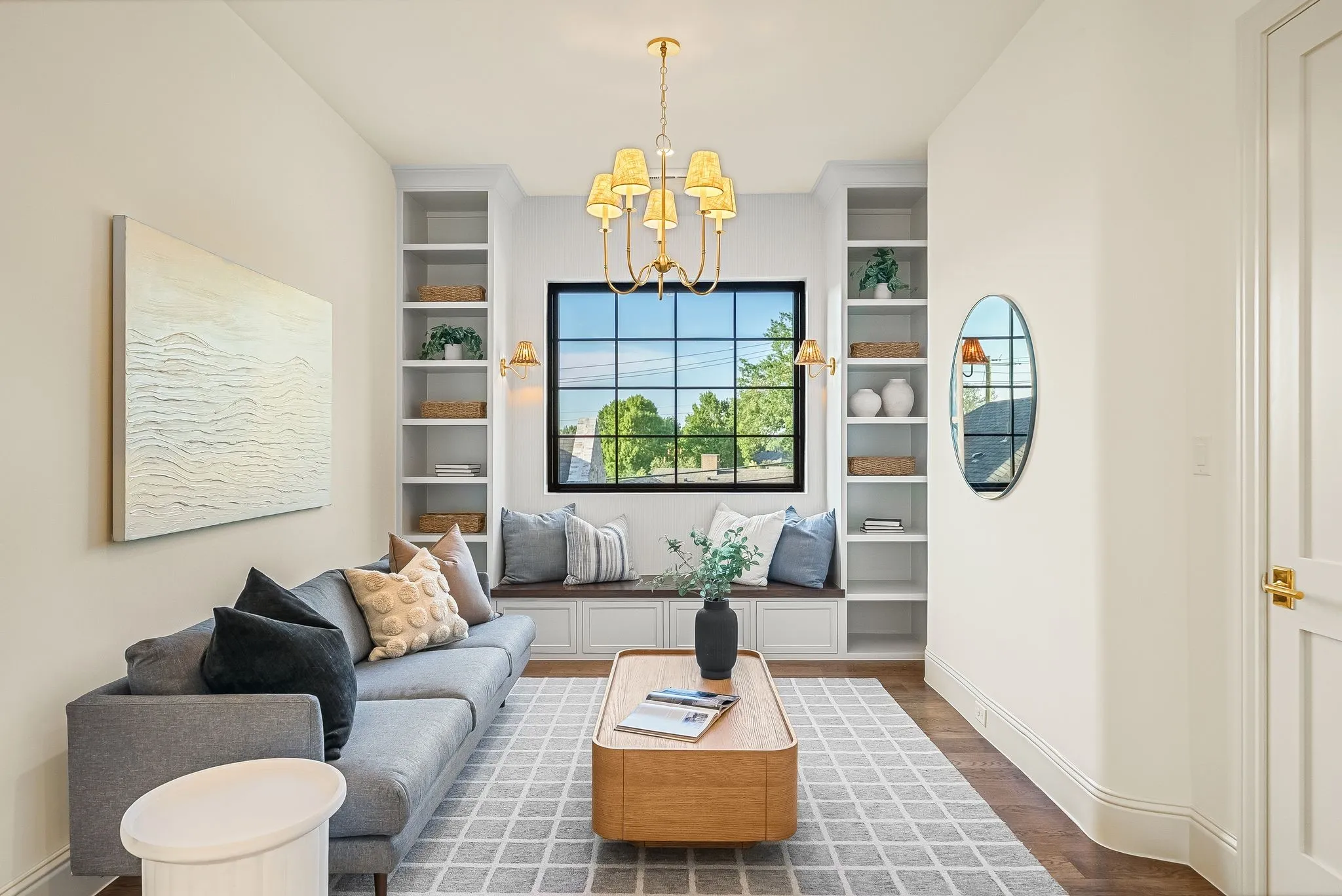 Built-in shelving, window bench seating, large grid-pattern window, wood-finish flooring, and a decorative chandelier