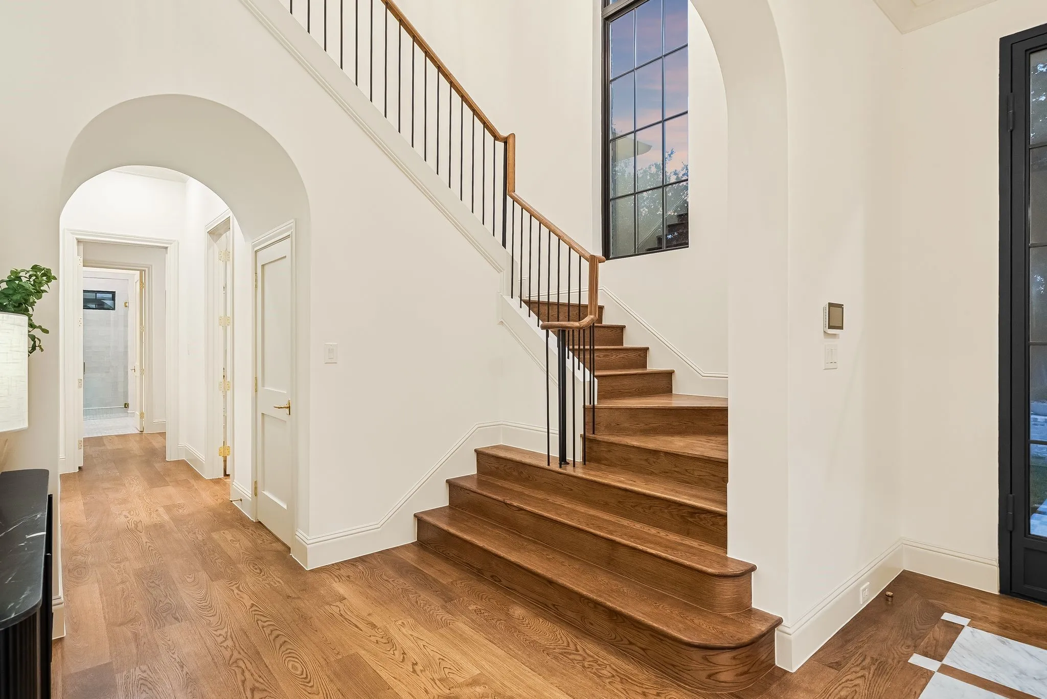 Hardwood flooring, arched doorway, custom staircase with wood handrail and black metal balusters, and a large grid-pattern window