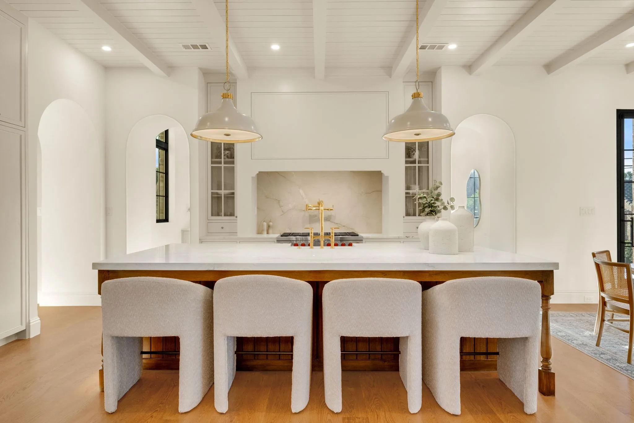 Exposed beam ceiling with recessed lighting and pendant fixtures, kitchen island with seating, built-in cabinetry with glass inserts, and arched doorways