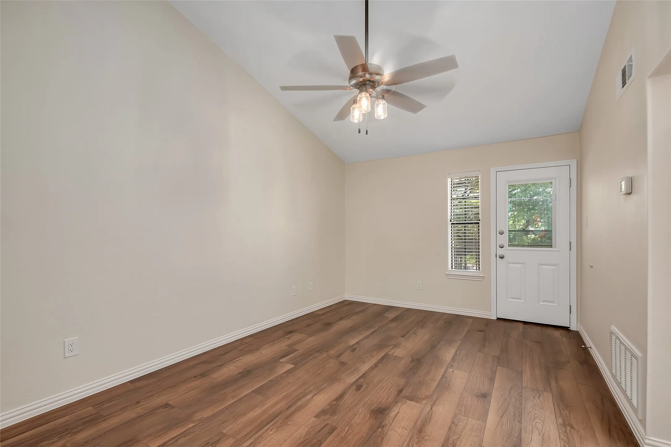 Vaulted ceiling with a ceiling fan, wood-finish flooring, white paneled door with glass insert, and a window with blinds
