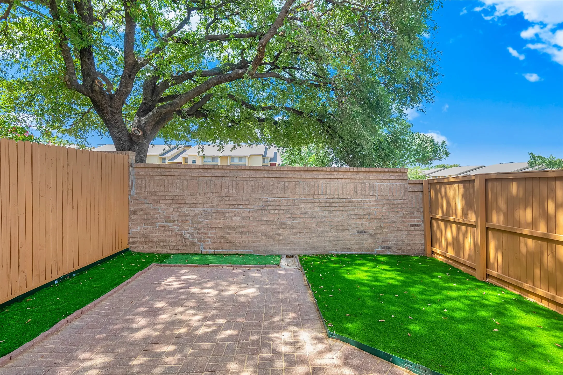 Private outdoor space featuring a paver patio, artificial turf, wood fencing, and a brick privacy wall
