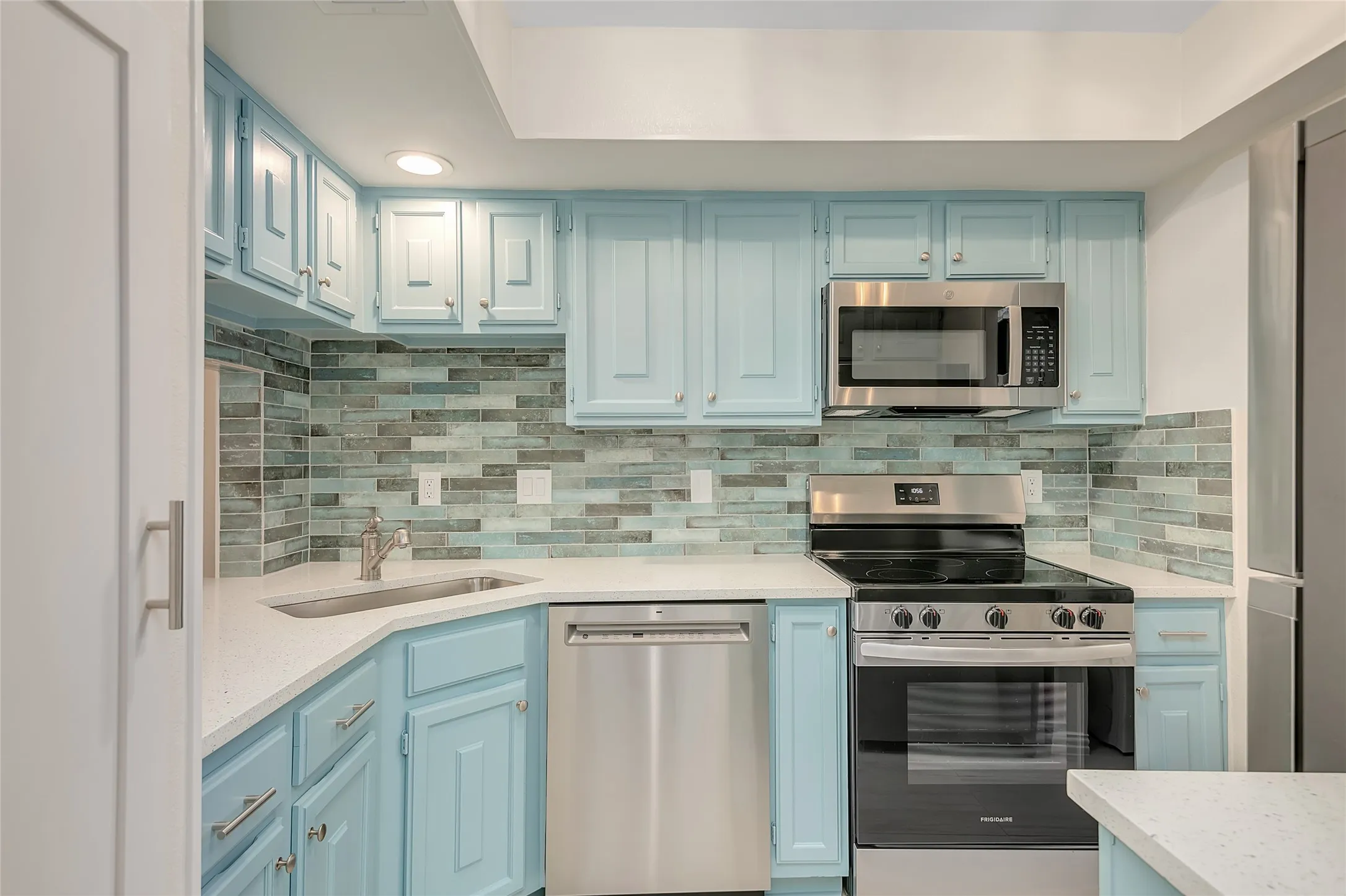 Kitchen featuring light blue cabinetry, stainless steel appliances, white countertops, and a full-height tile backsplash