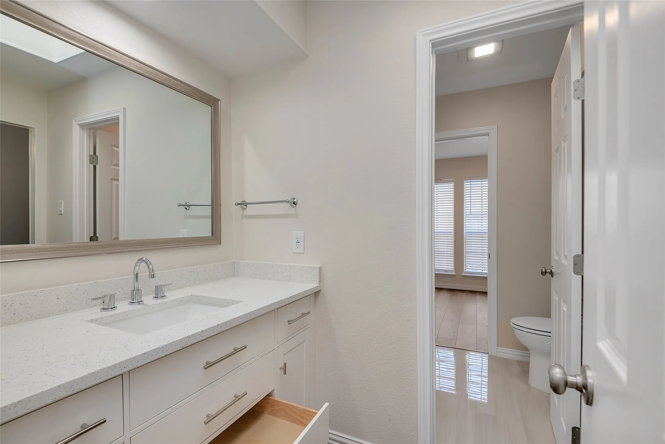 White vanity with ample storage, quartz countertop, chrome faucet, and rectangular framed mirror