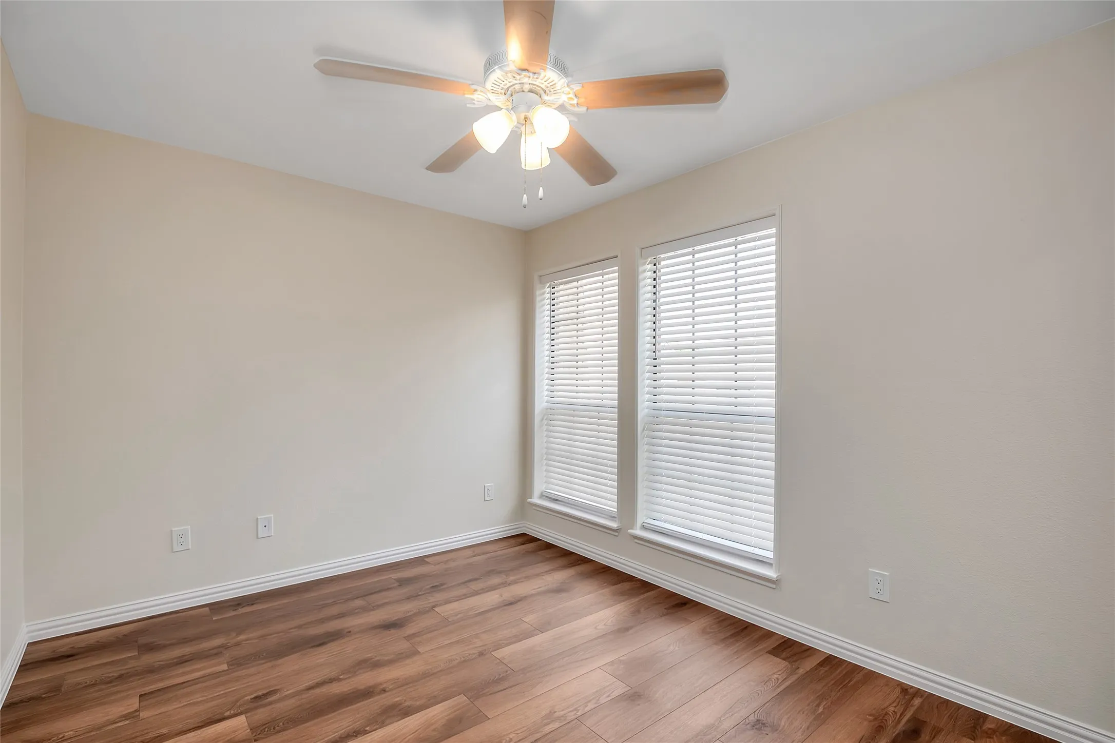 Wood-finish flooring, two windows with blinds, ceiling fan with light fixture, and light-colored walls