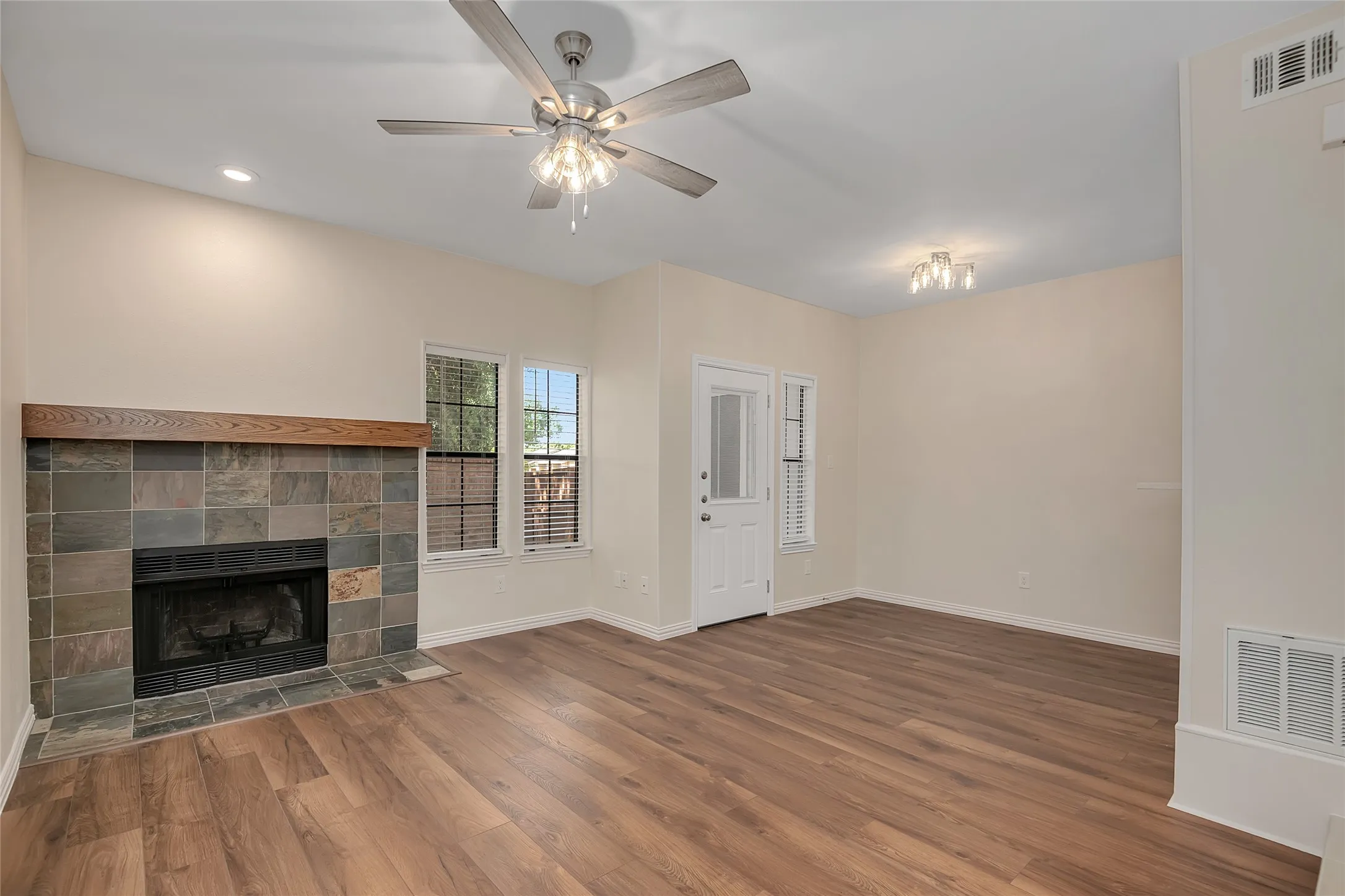Spacious interior featuring wood-finish flooring, a tile-surround fireplace with a wood mantel, and multiple windows for natural light