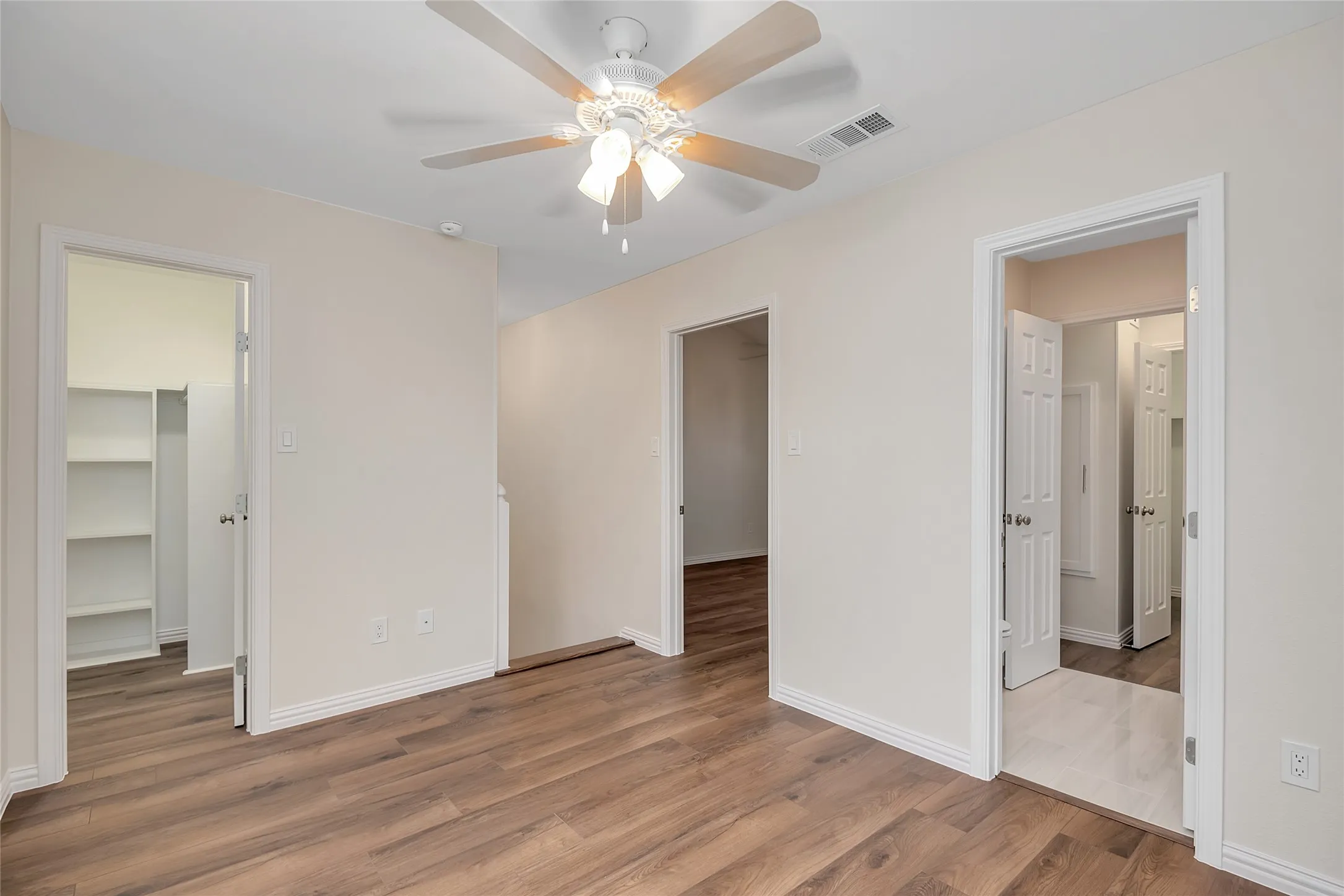 Wood-finish flooring, ceiling fan with integrated lighting, multiple doorways, and neutral wall tones