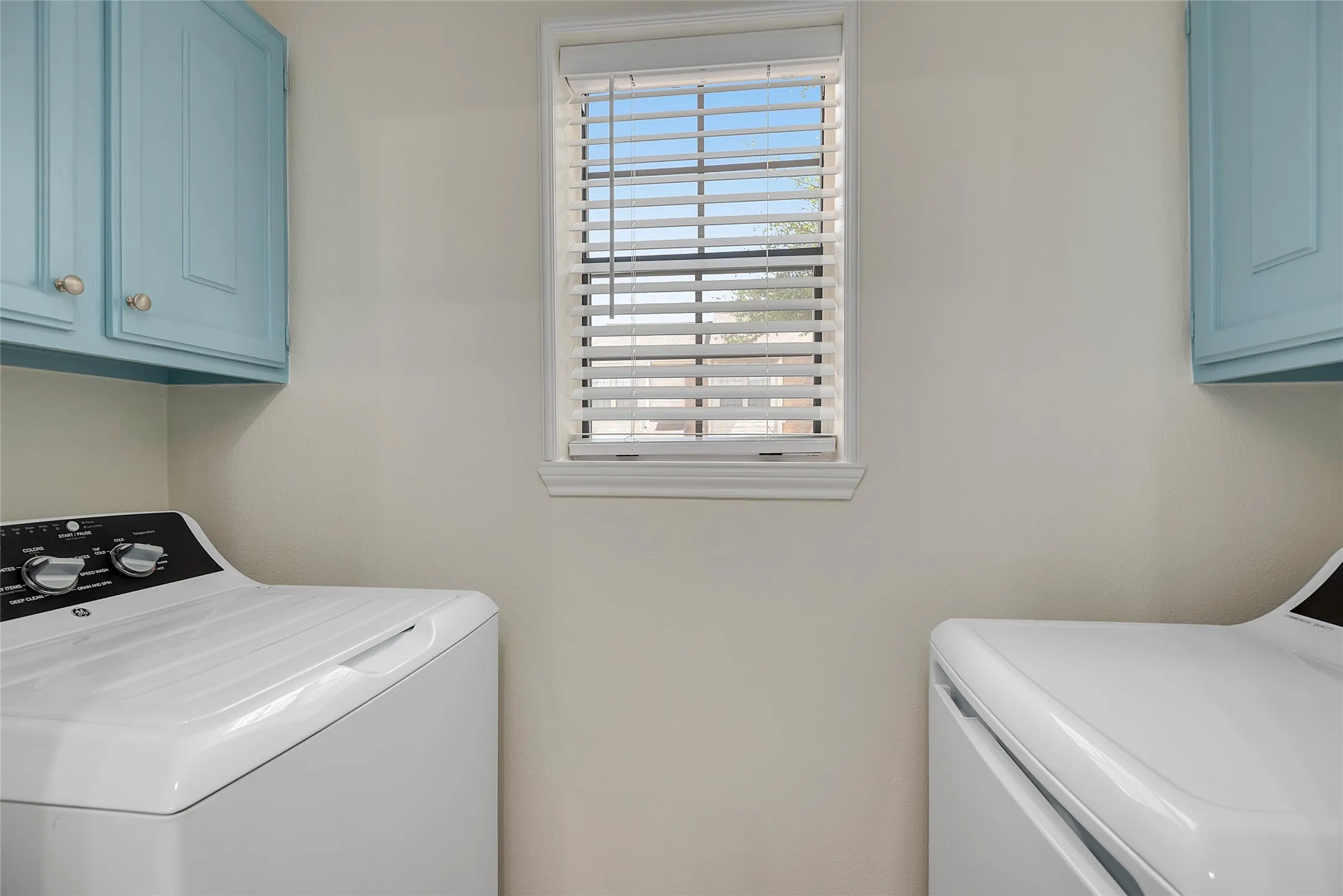 Built-in blue cabinetry with knob hardware, window with blinds, light wall paint color