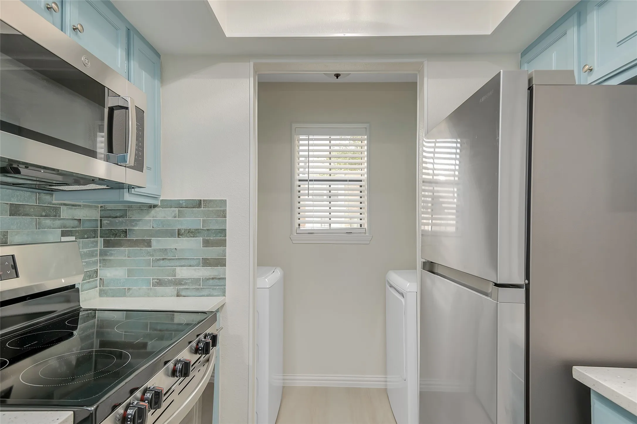 Stainless steel appliances, electric range with oven, built-in microwave, blue cabinetry, and a subway tile backsplash
