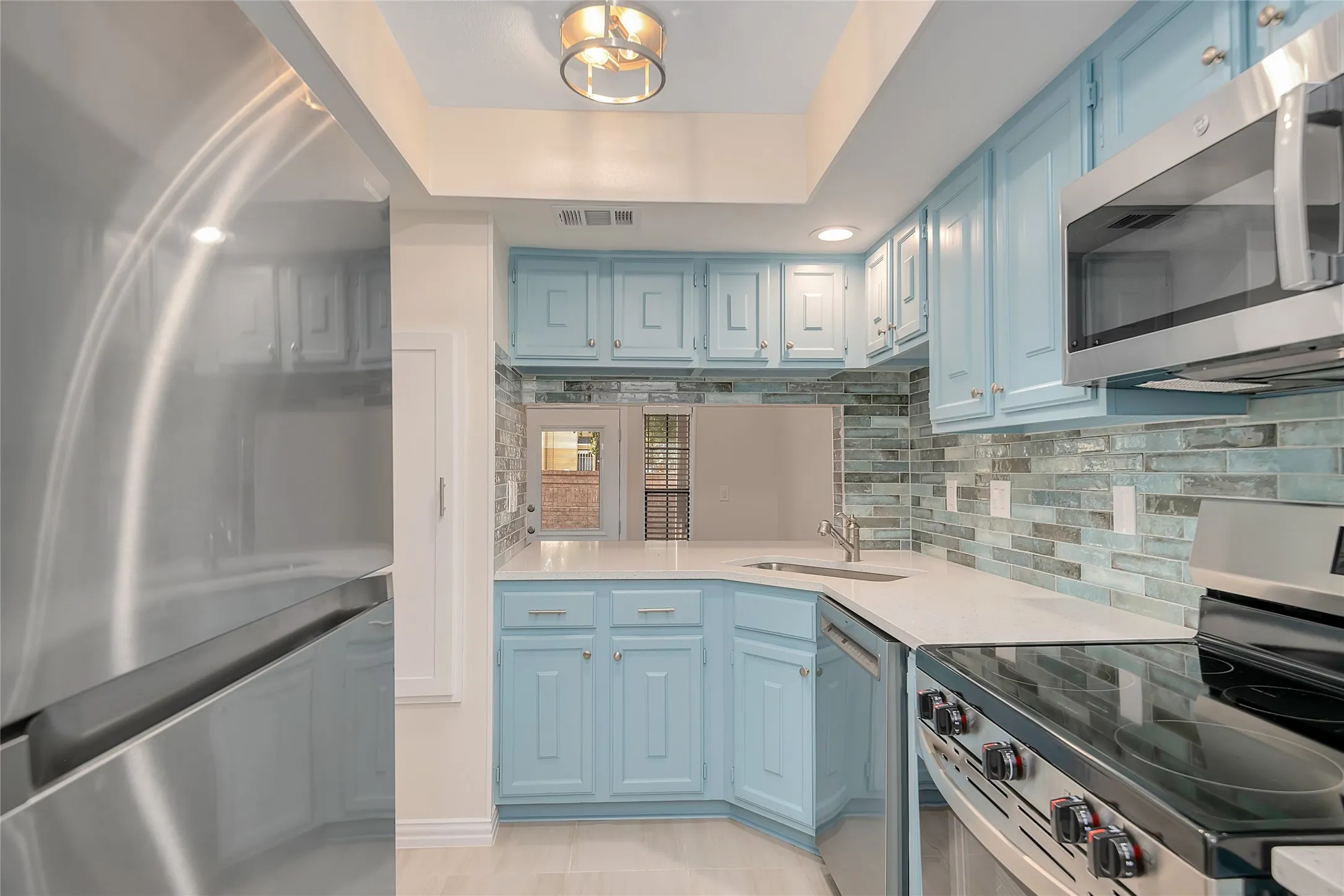 Light blue cabinetry with silver hardware, white countertops, glass tile backsplash, stainless steel appliances, and a recessed ceiling light fixture