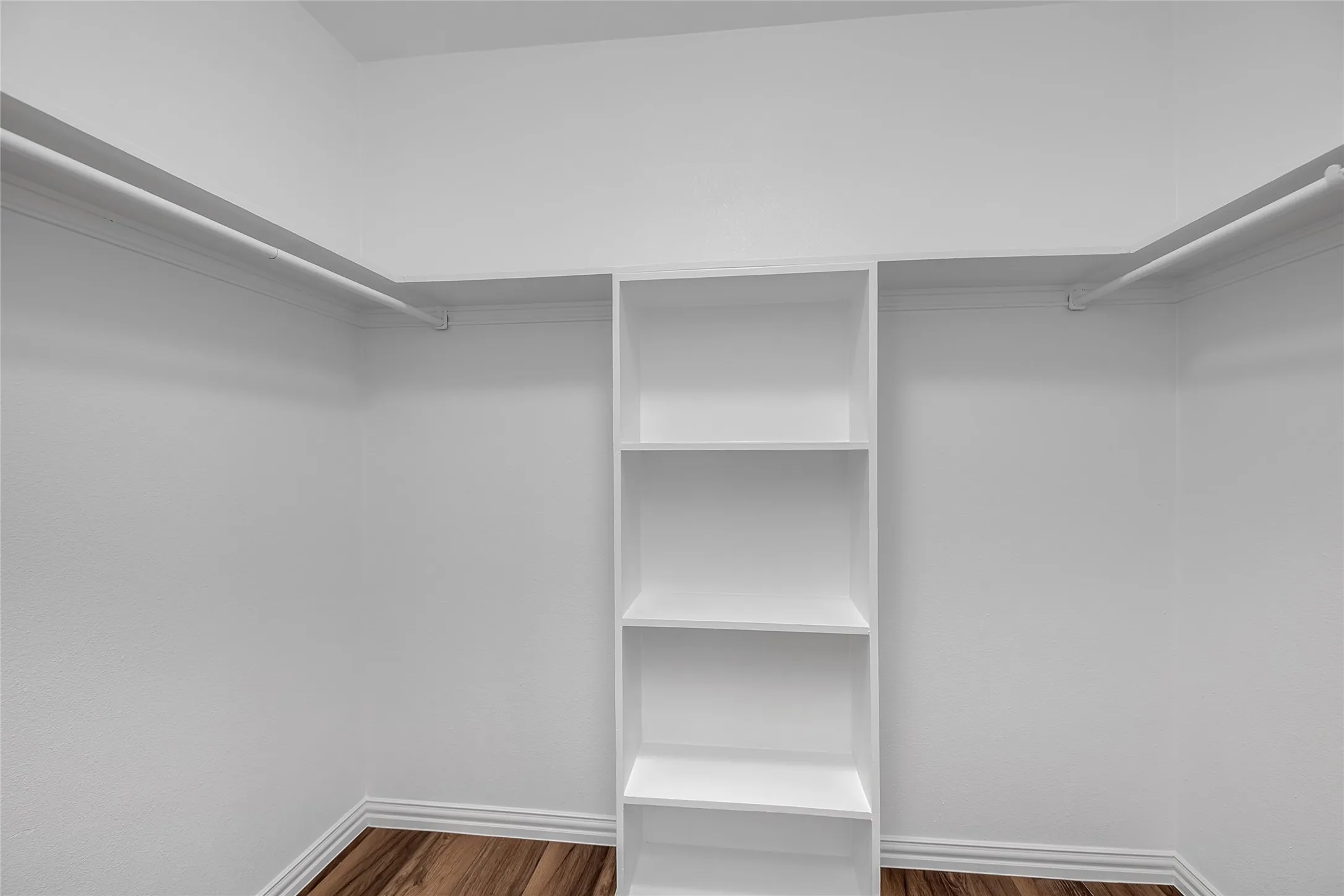 White walk-in closet featuring built-in shelving, multiple hanging rods, and wood-finish flooring