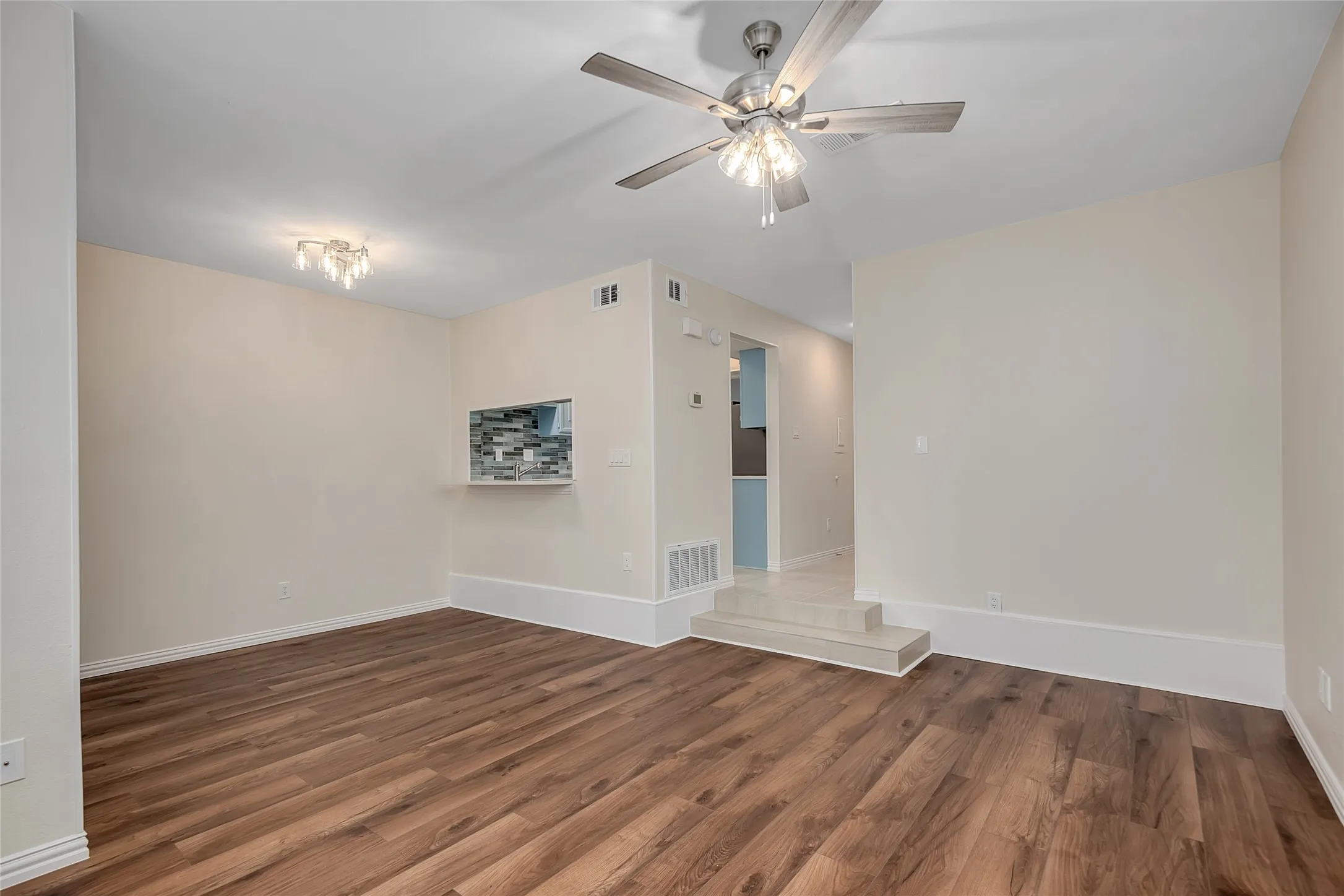Spacious room with wood-finish flooring, a contemporary ceiling fan, and a pass-through opening with mosaic tile