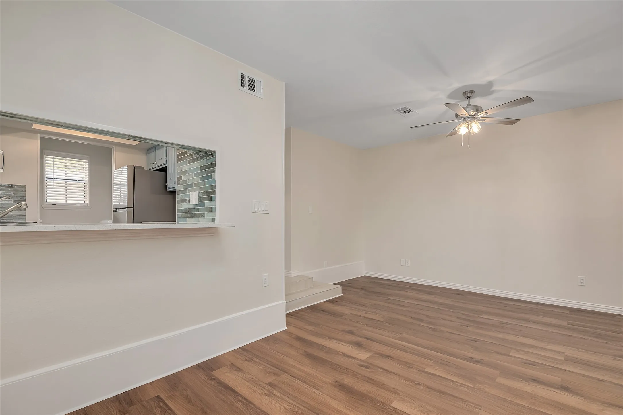 Wood-finish flooring, ceiling fan with integrated lighting, pass-through window with countertop, and subway tile backsplash