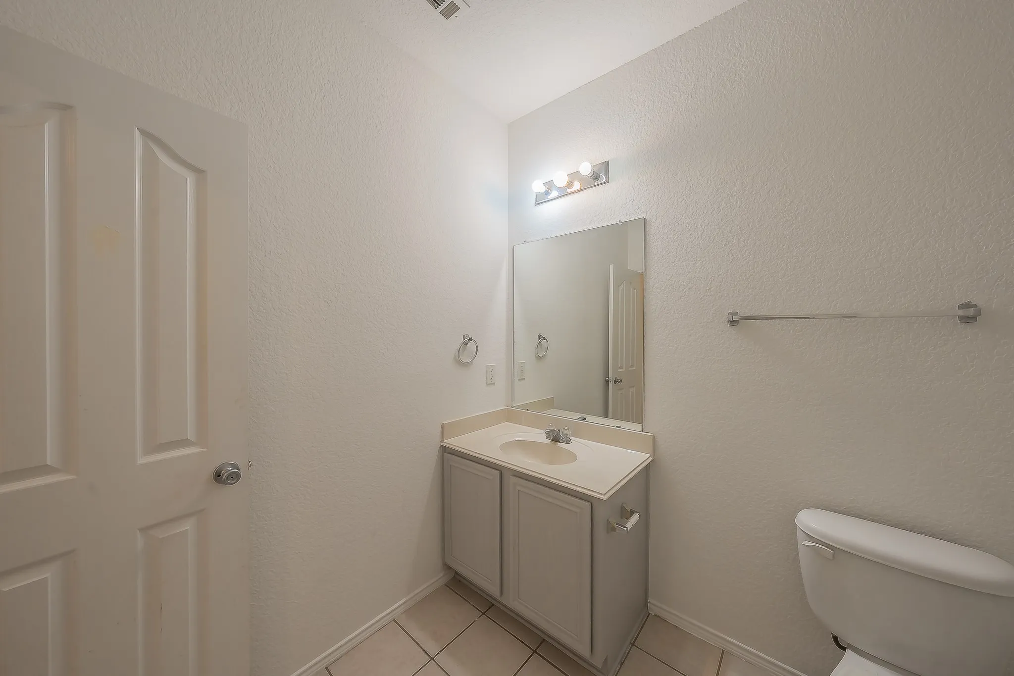 White paneled door, light-toned vanity with an integrated sink, wall-mounted mirror, and tile flooring