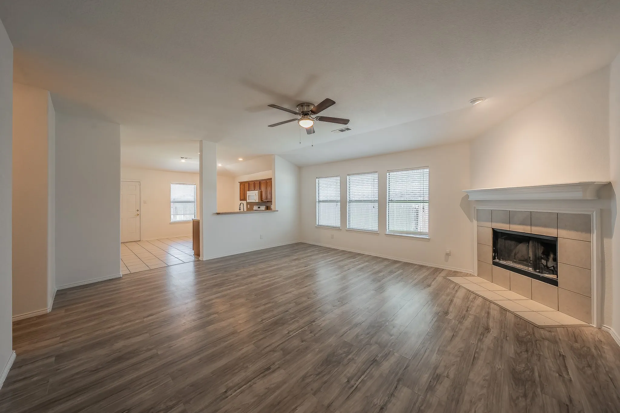 Spacious living area featuring wood-finish flooring, a ceiling fan, and multiple windows